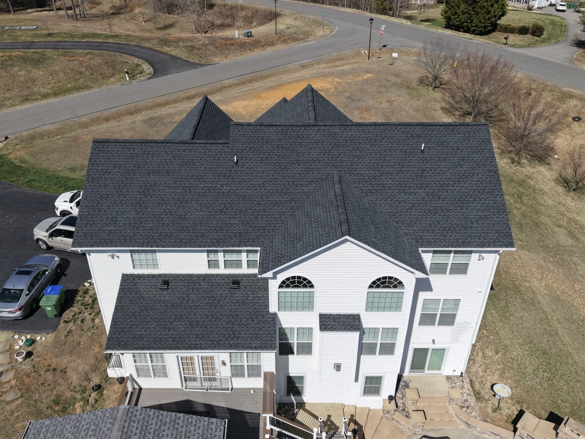 Aerial view of a large white house with a dark roof beside a road in a rural area