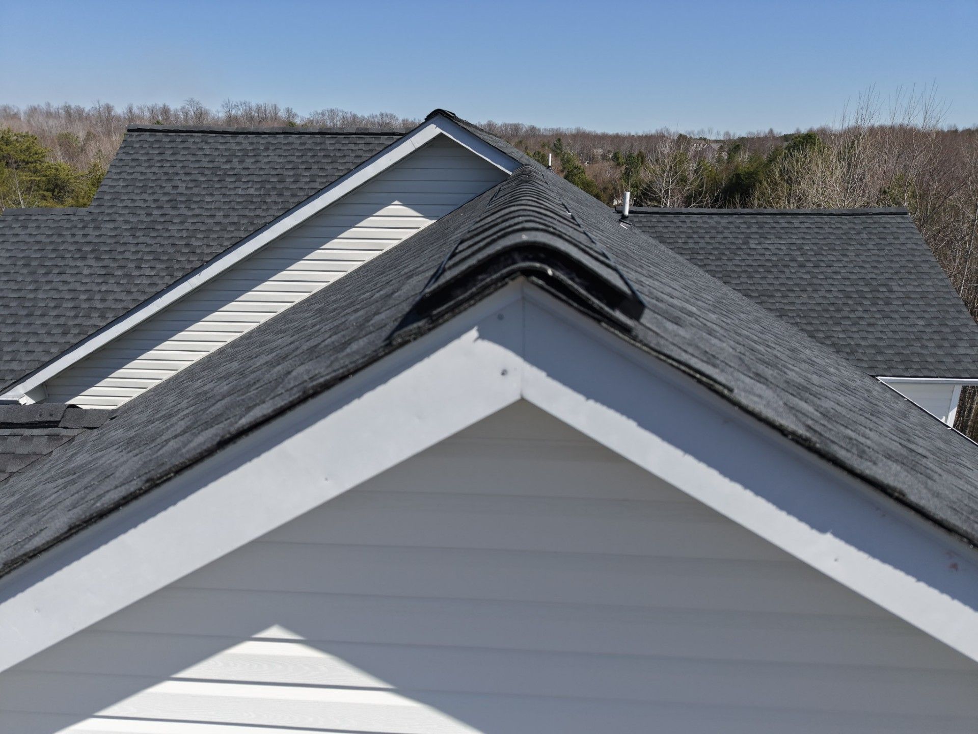 Close-up of house rooftops with gray shingles and white gable trim under a clear blue sky