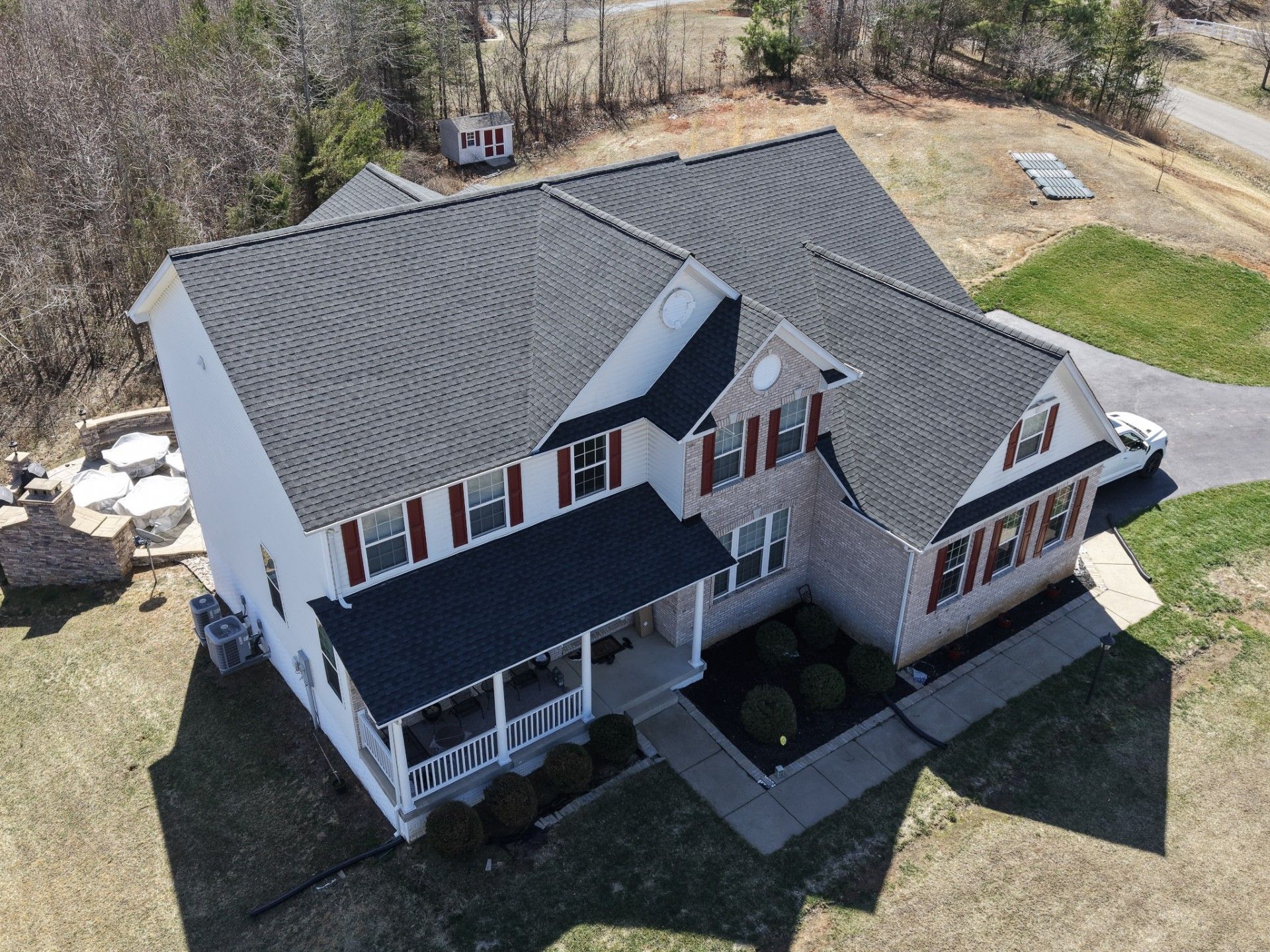 Aerial view of a two-story house with a dark roof, white siding, and red shutters on a grassy lot.