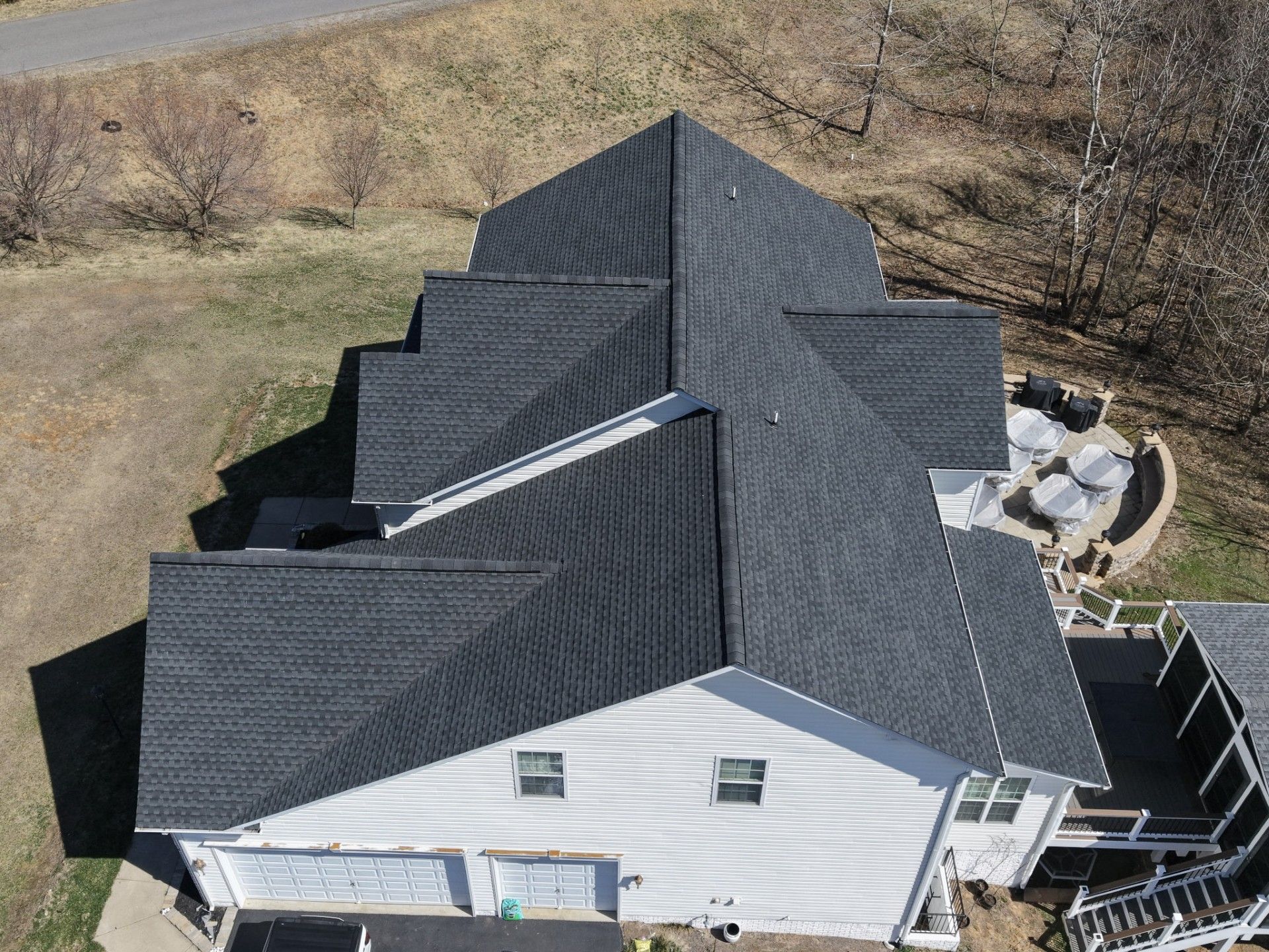 Aerial view of a house with a dark gray roof and white siding, surrounded by a yard.