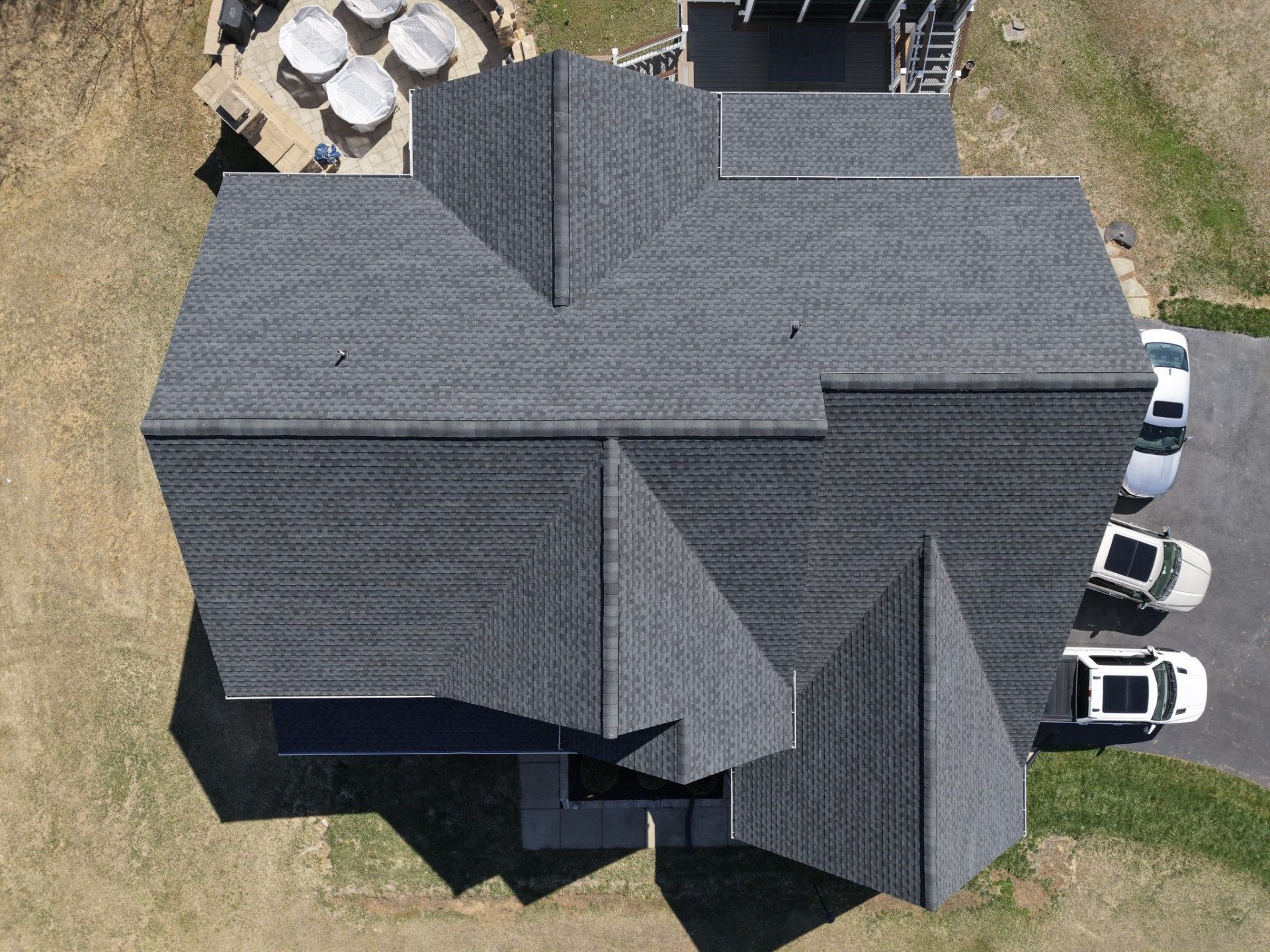 Aerial view of a gray-roofed house with parked cars and a patio area nearby.