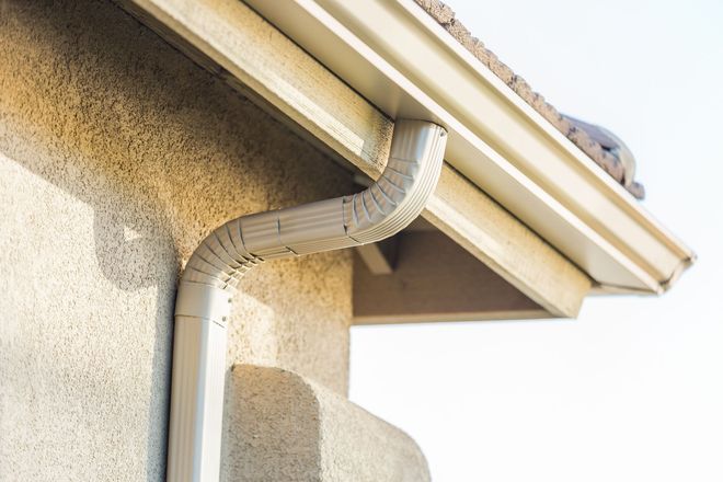 House gutter downspout on beige stucco wall beneath roof eaves