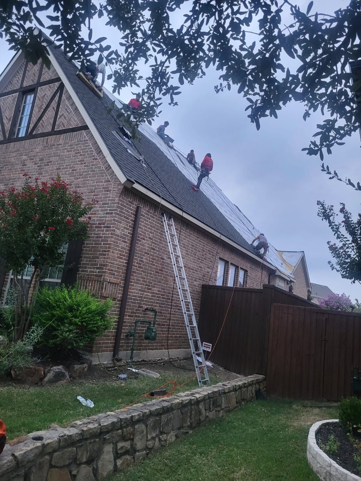 Brick house roof under repair with workers on top and a ladder against the wall