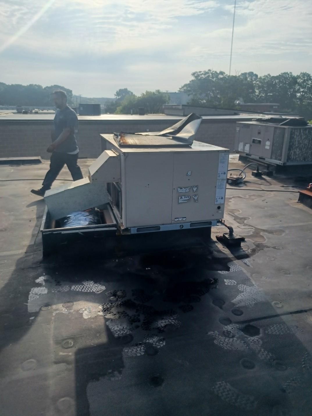 Person walking past an HVAC unit on a flat rooftop.