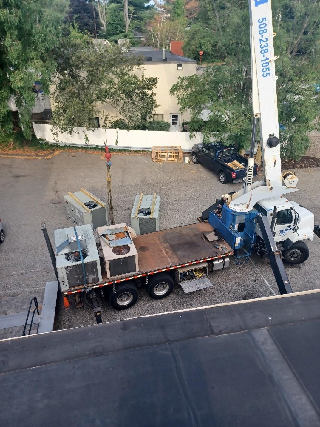 Crane truck lifting HVAC units from a flatbed in a parking lot.