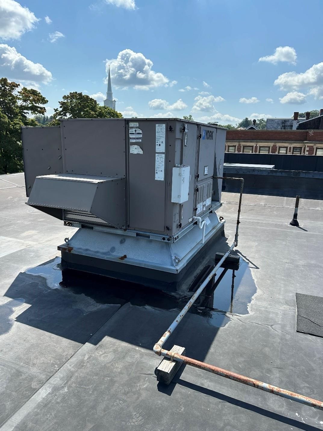 Rooftop HVAC unit on a flat roof with a church steeple in the background on a sunny day.