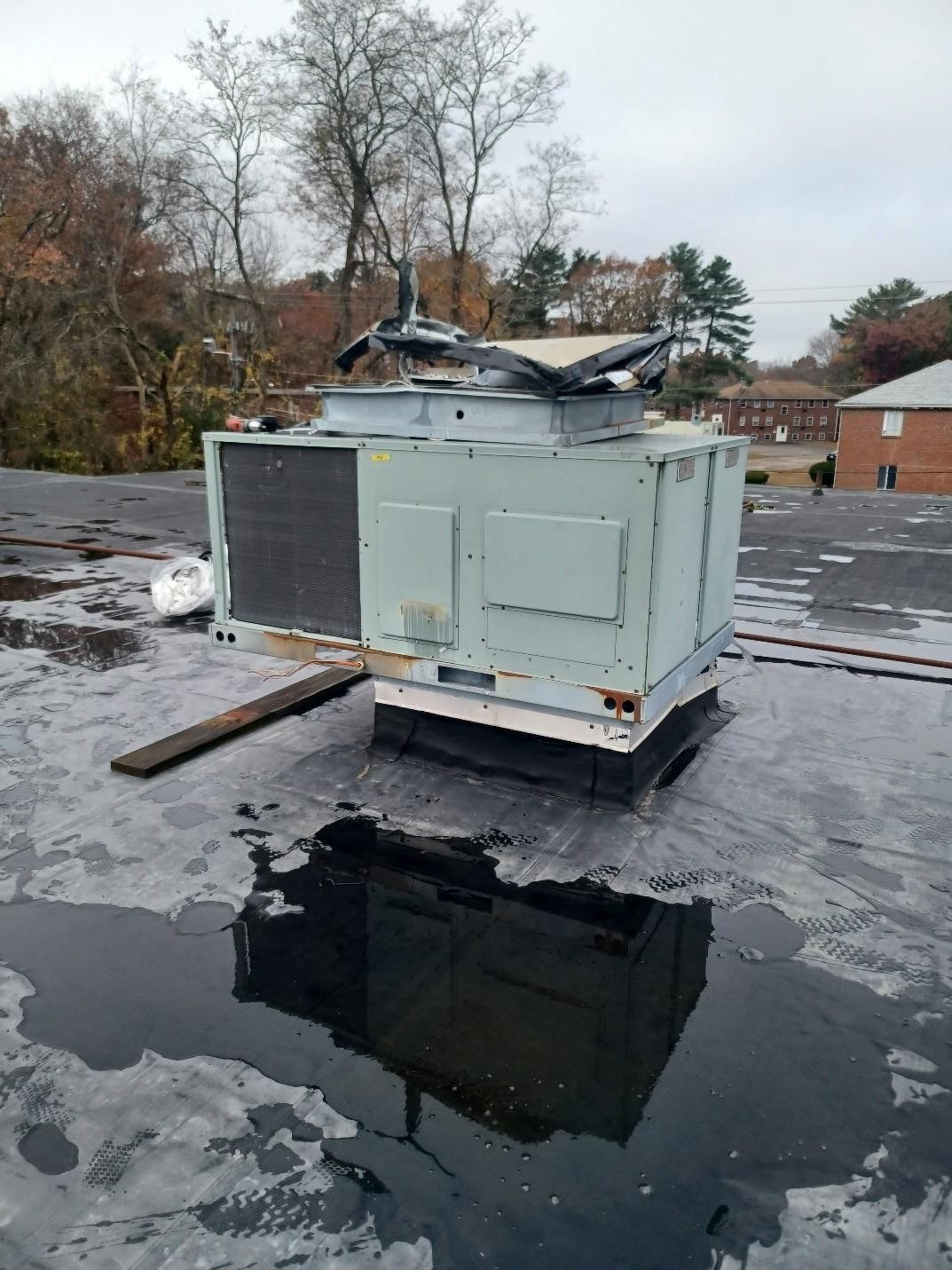 HVAC unit on a flat roof, surrounded by standing water, overcast sky.