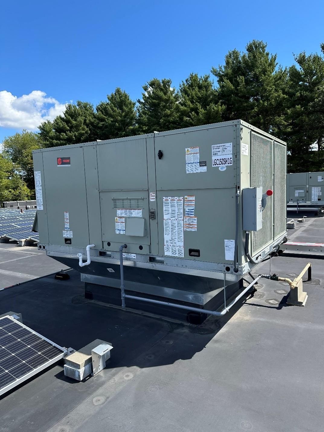 HVAC unit on a rooftop with a blue sky and trees in the background.