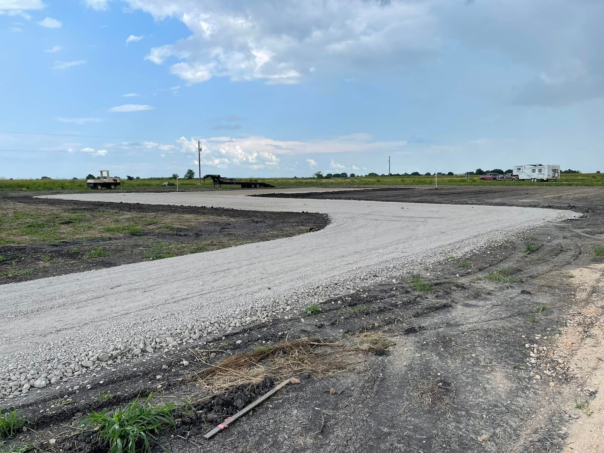 Gravel driveway curves through a field under a blue sky with some clouds.