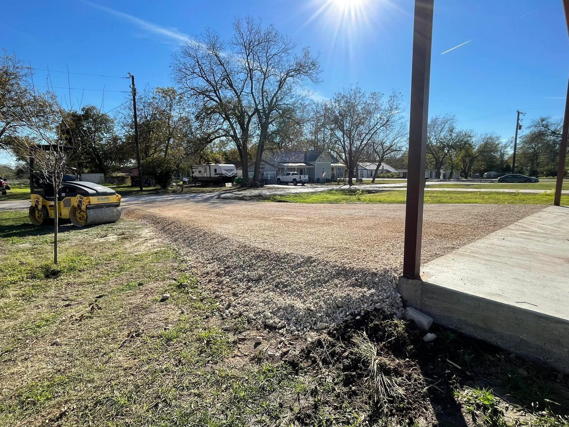Construction site with gravel driveway, roller, grass, blue sky.