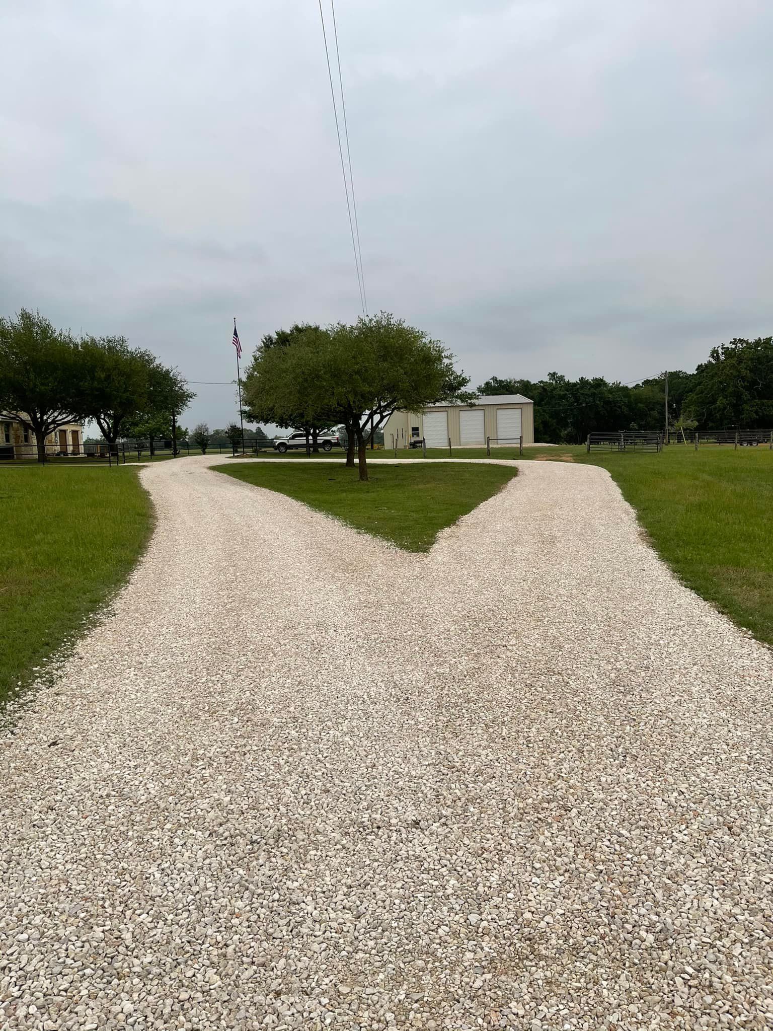 Gravel paths split in a Y-shape through a grassy area with trees and buildings under a cloudy sky.