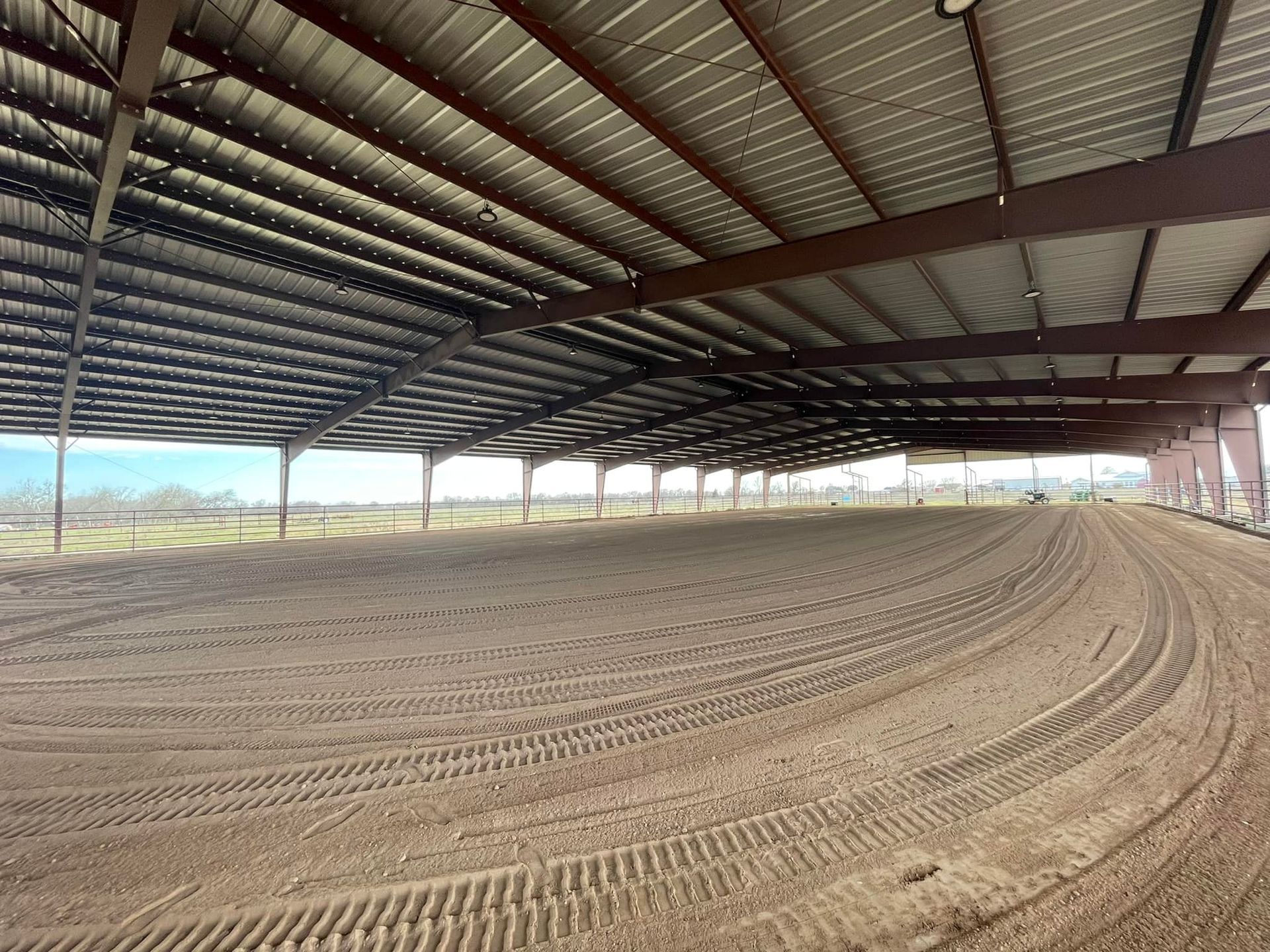 Indoor equestrian arena with a dirt floor under a metal roof.
