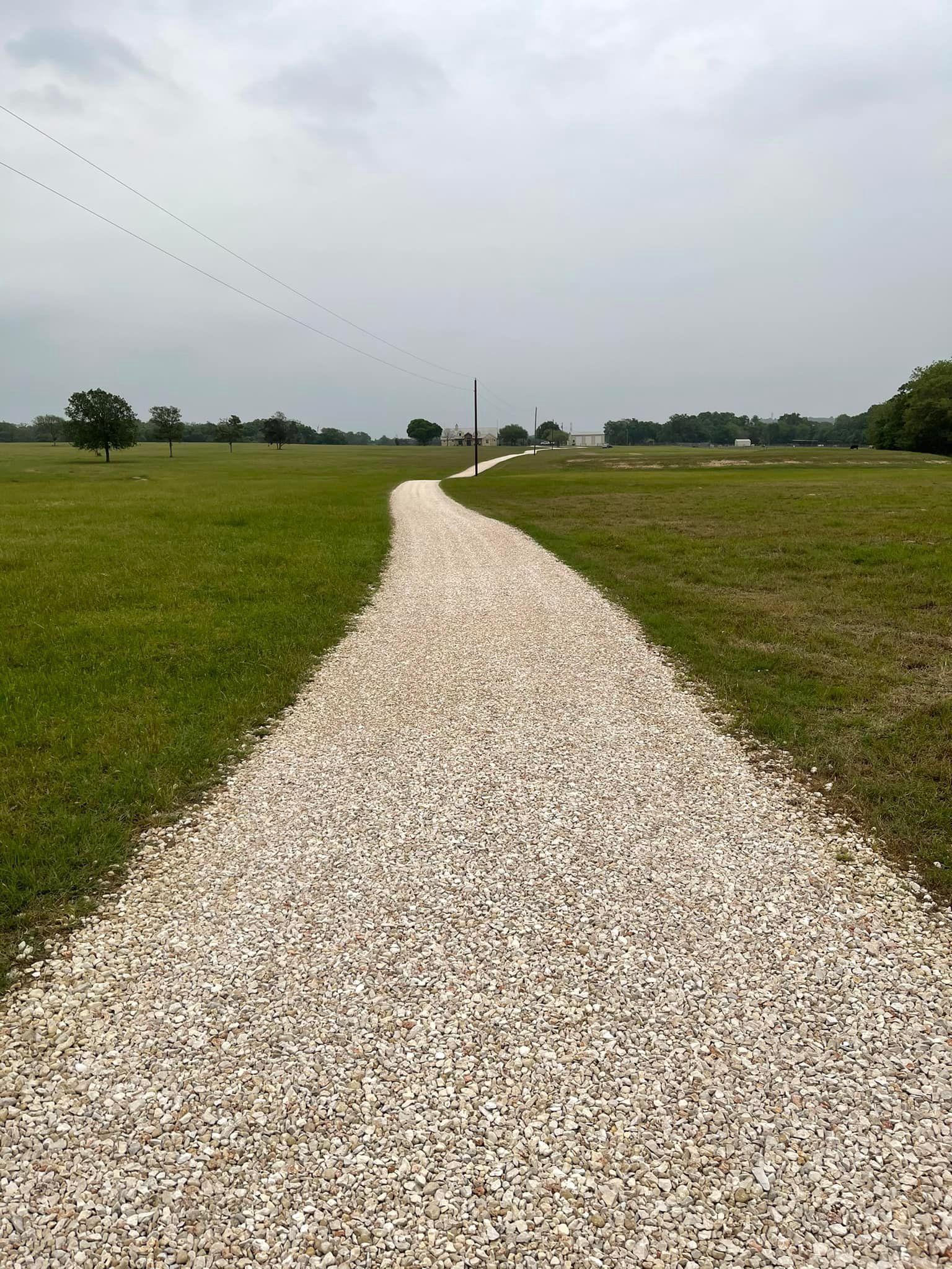Gravel path through green field towards tall white monument under overcast sky.