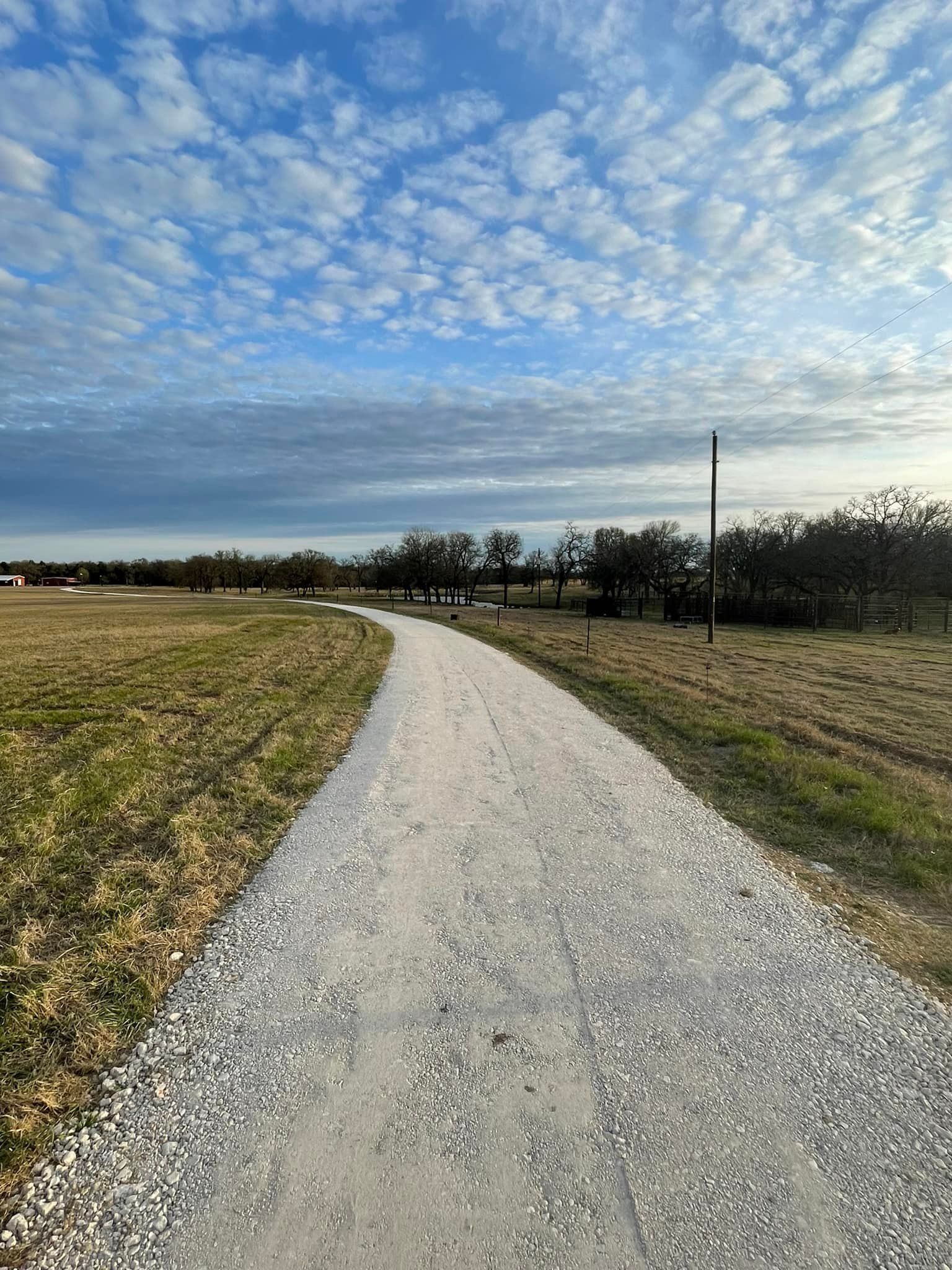 A gravel path winds through a grassy field, under a cloudy blue sky.
