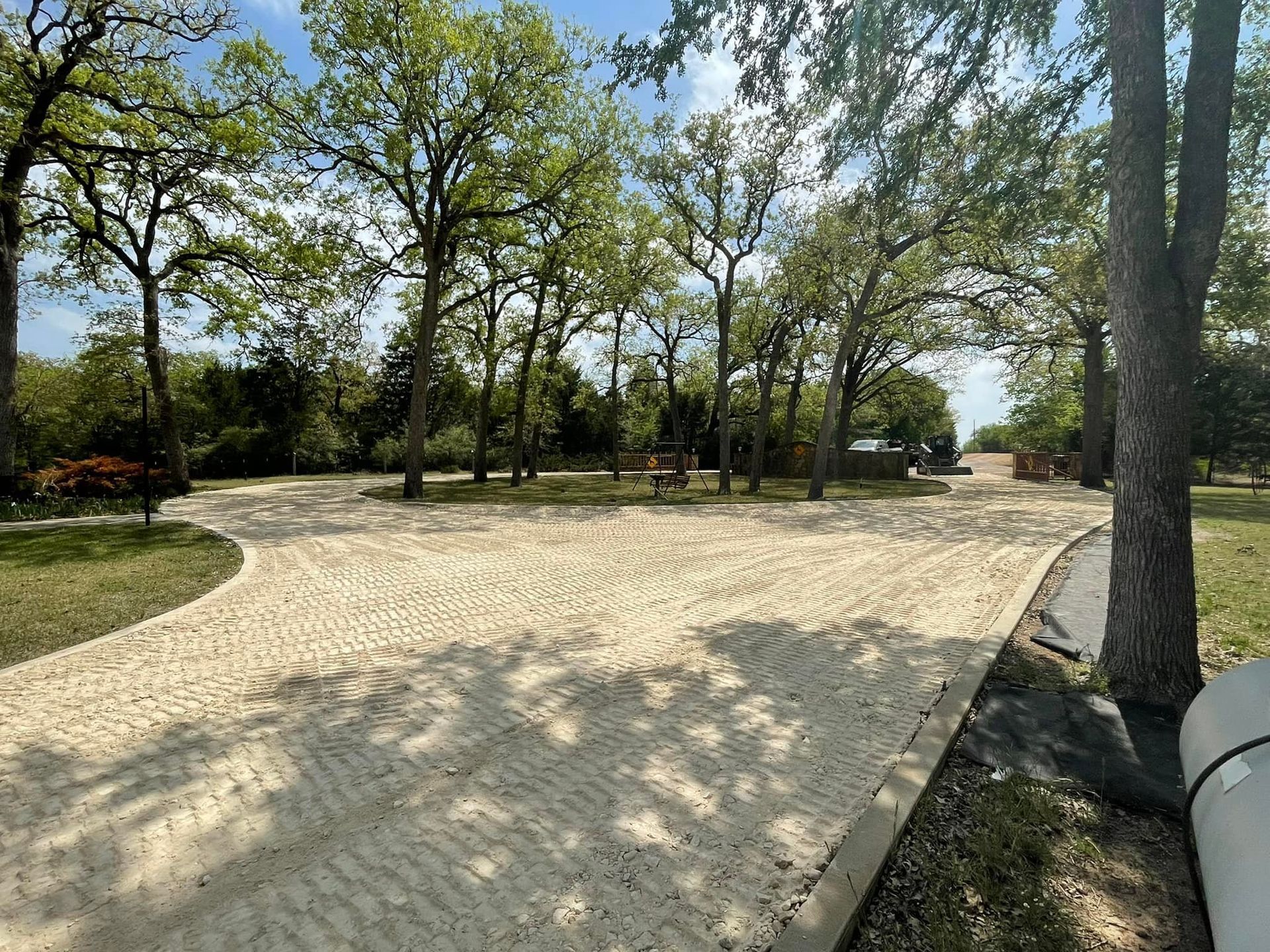 Gravel road forks into a campground, shaded by trees on a sunny day.