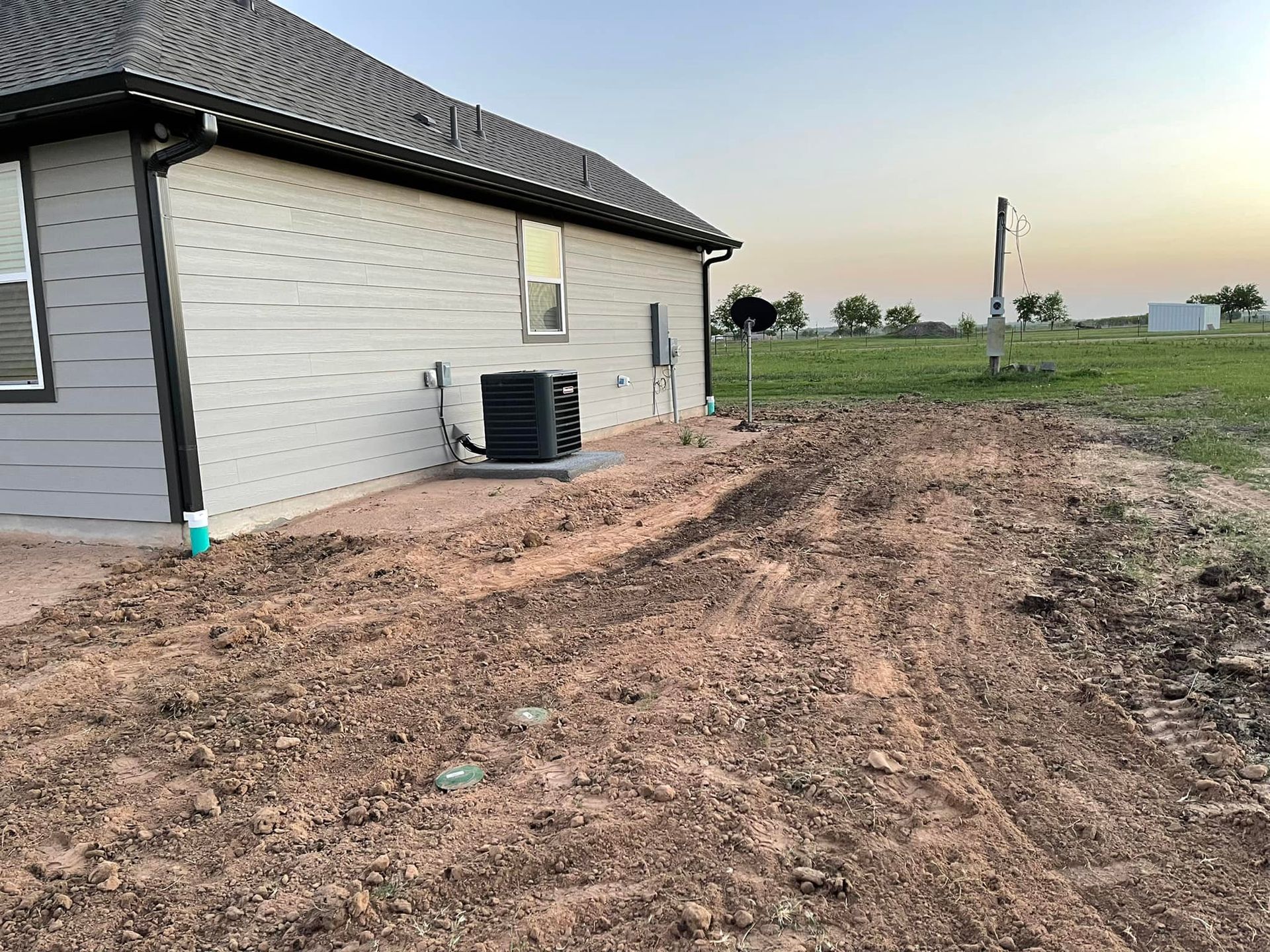 Backyard of a house with dirt ground, air conditioning unit.