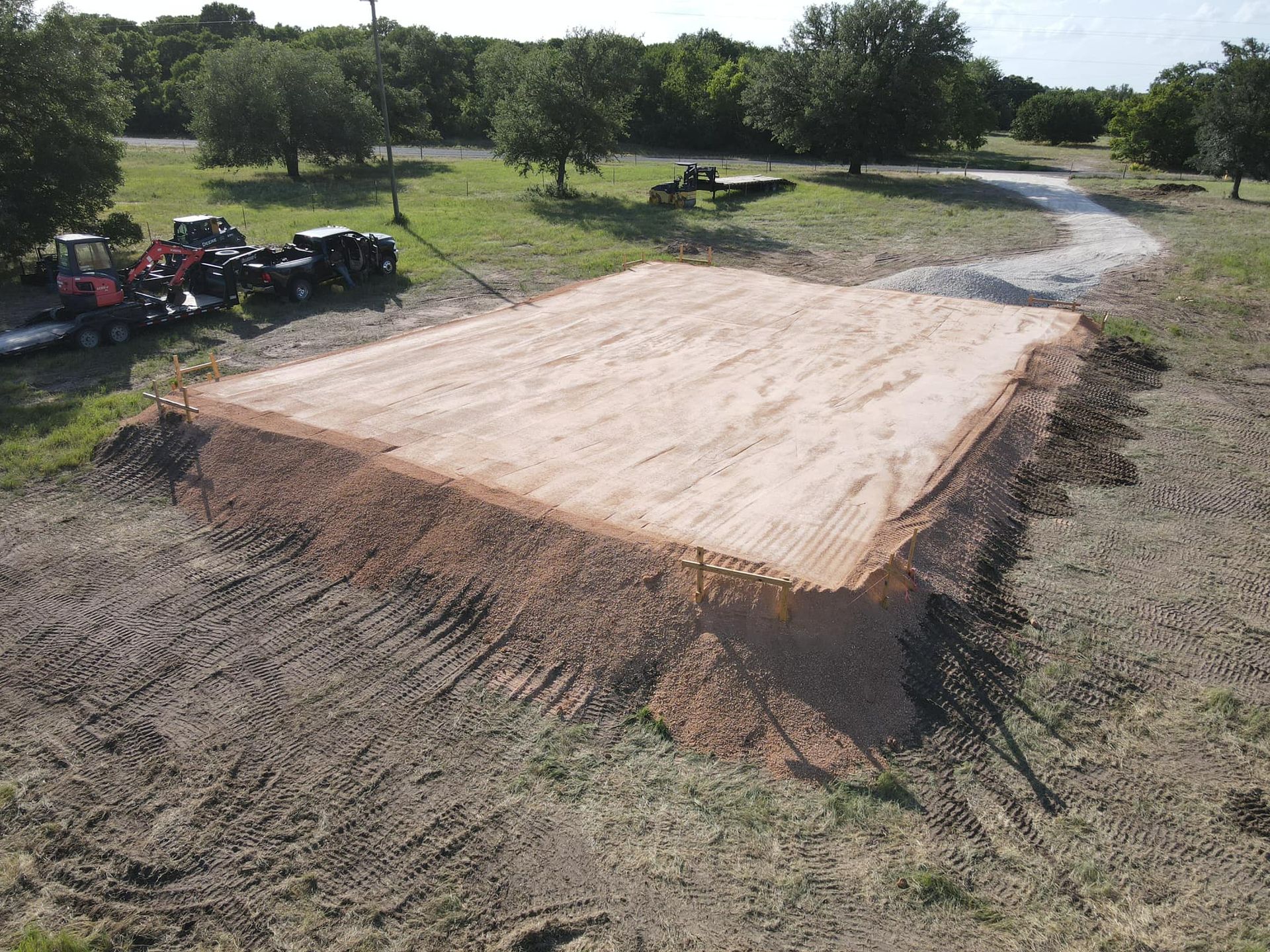 Aerial view: A rectangular area of leveled dirt, with tractors nearby, set in a grassy field.