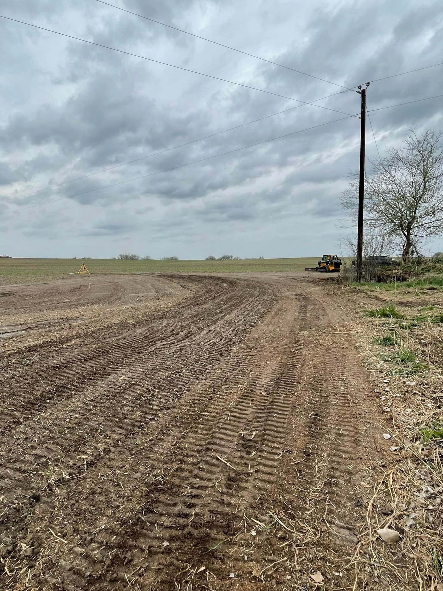 Muddy field with tractor tracks under cloudy sky, utility pole in the right.
