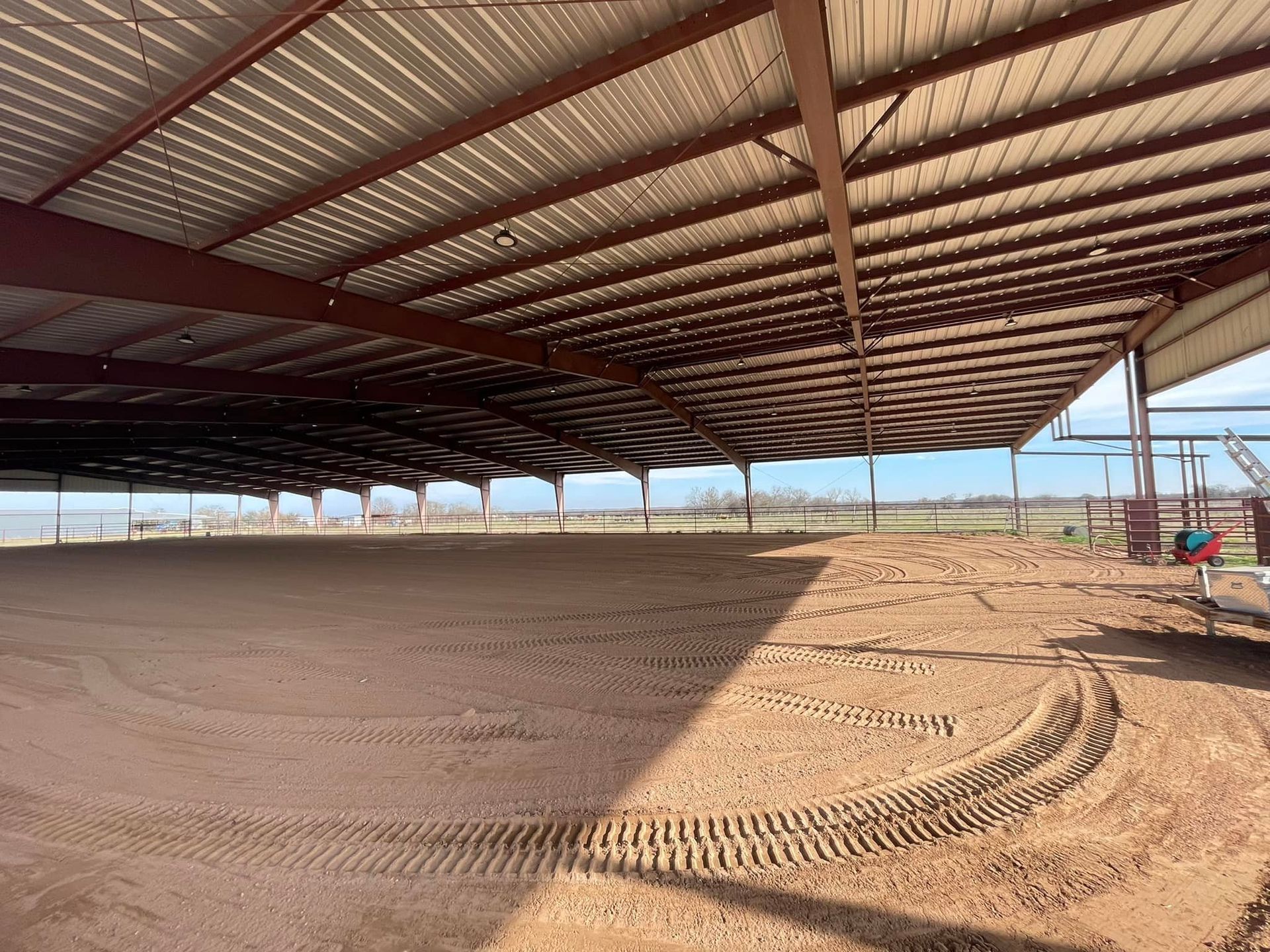 Large covered arena with dirt floor and tire tracks. Brown metal beams support the roof.