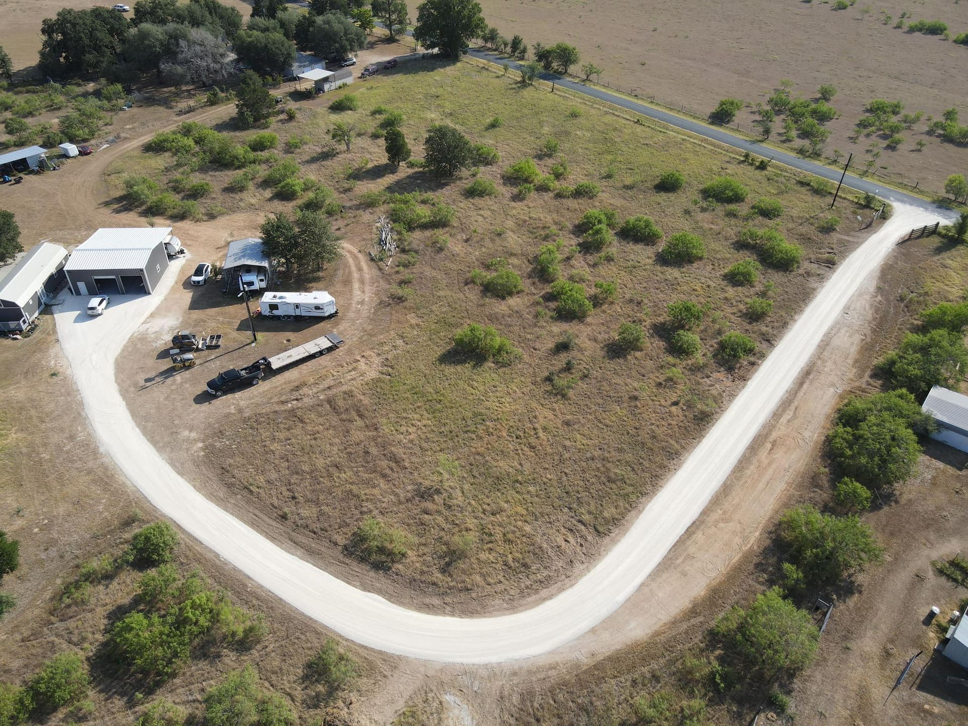Aerial view of a dirt road curving through a grassy field with scattered shrubs.