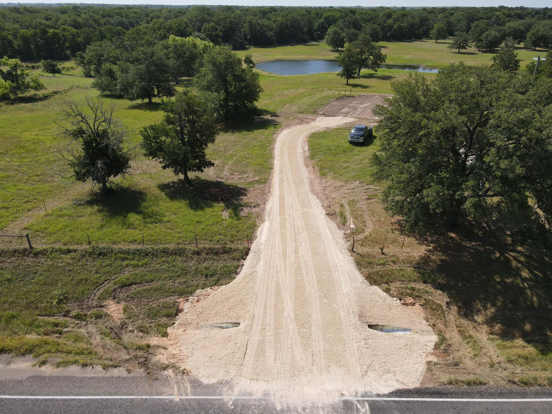 Gravel driveway leading from road into a field with trees, a small pond, and a truck.