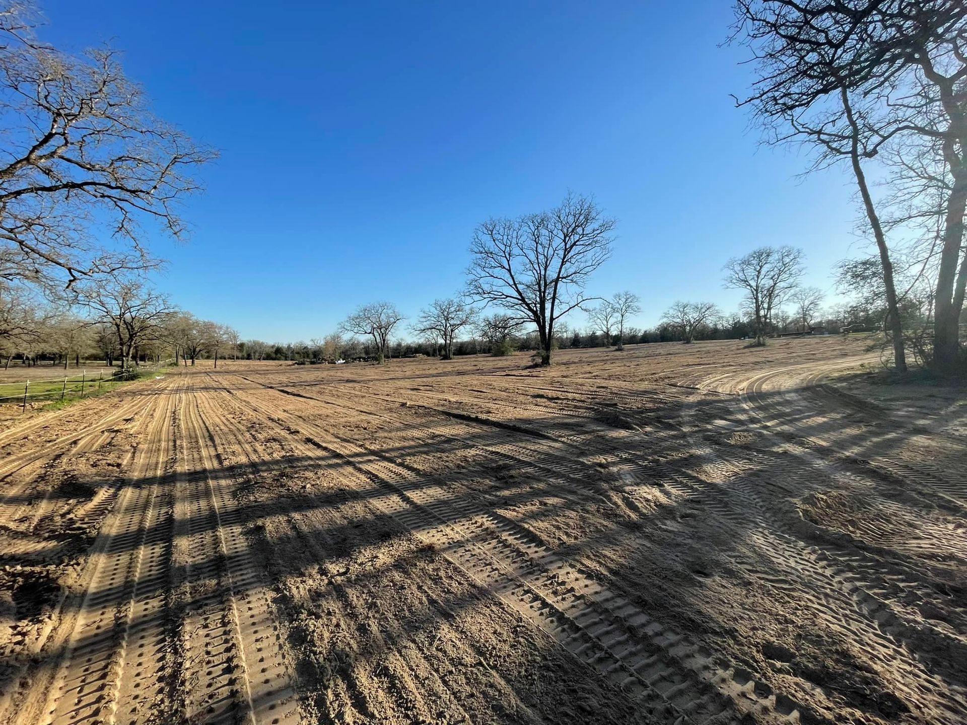 Cleared field with tire tracks, under a blue sky with bare trees.