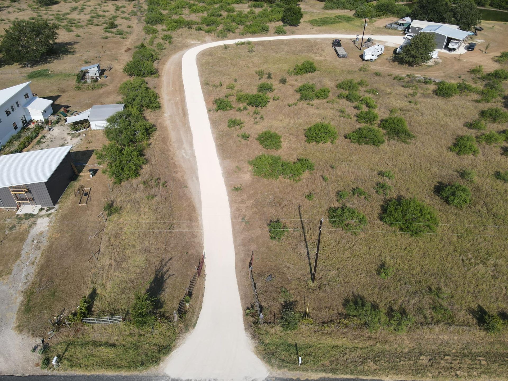 Aerial view of a gravel road curving through dry brush, with buildings on either side.