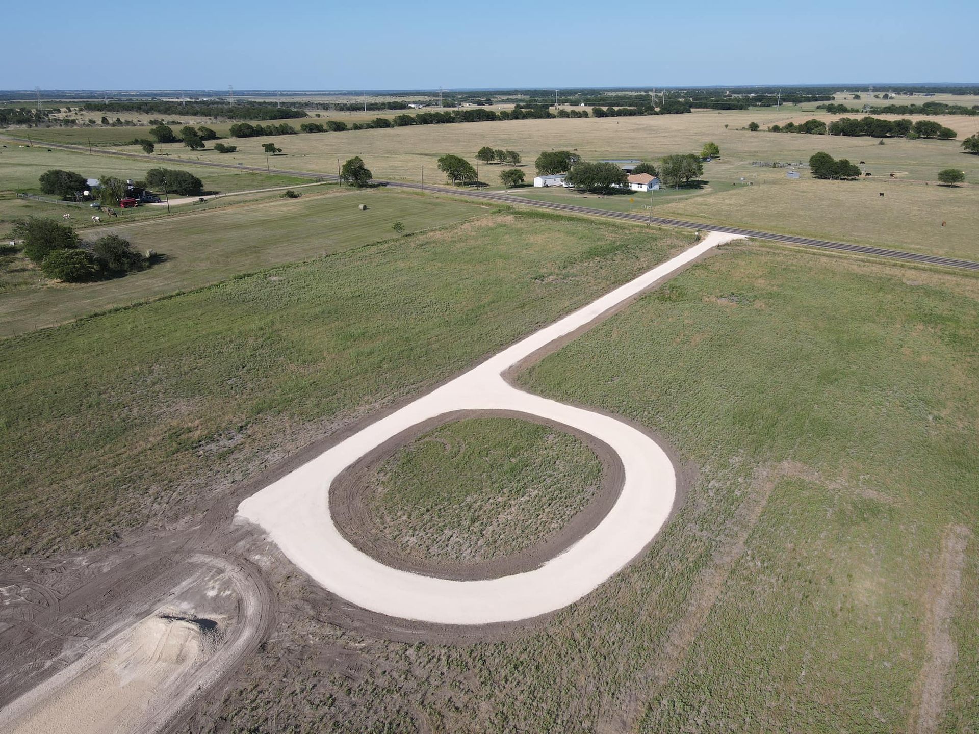 Aerial view: Gravel road in rural setting. Road curves in a loop, leading to a house in the distance.