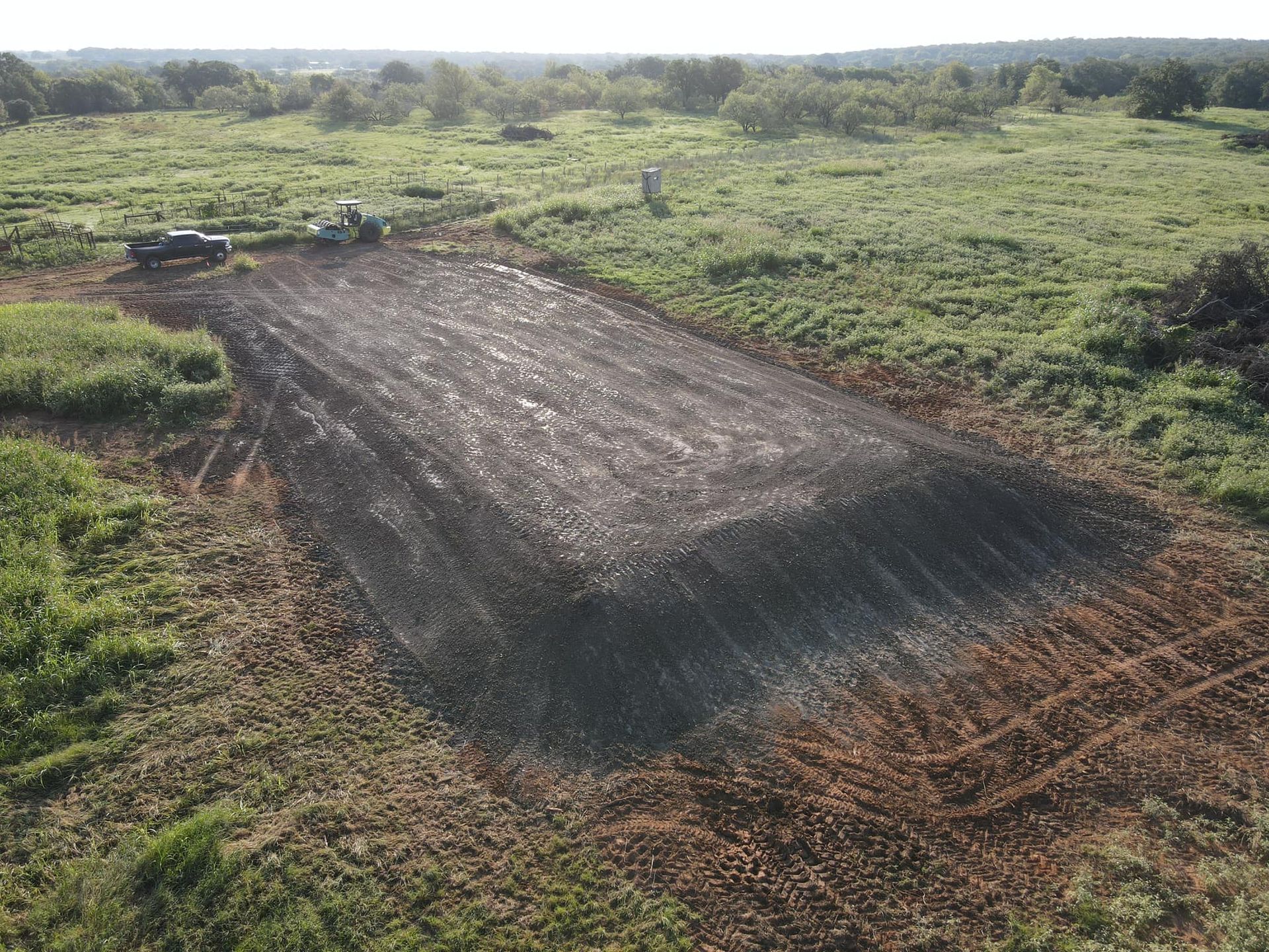 A field of dark material covering a large area with a tractor on the edge.