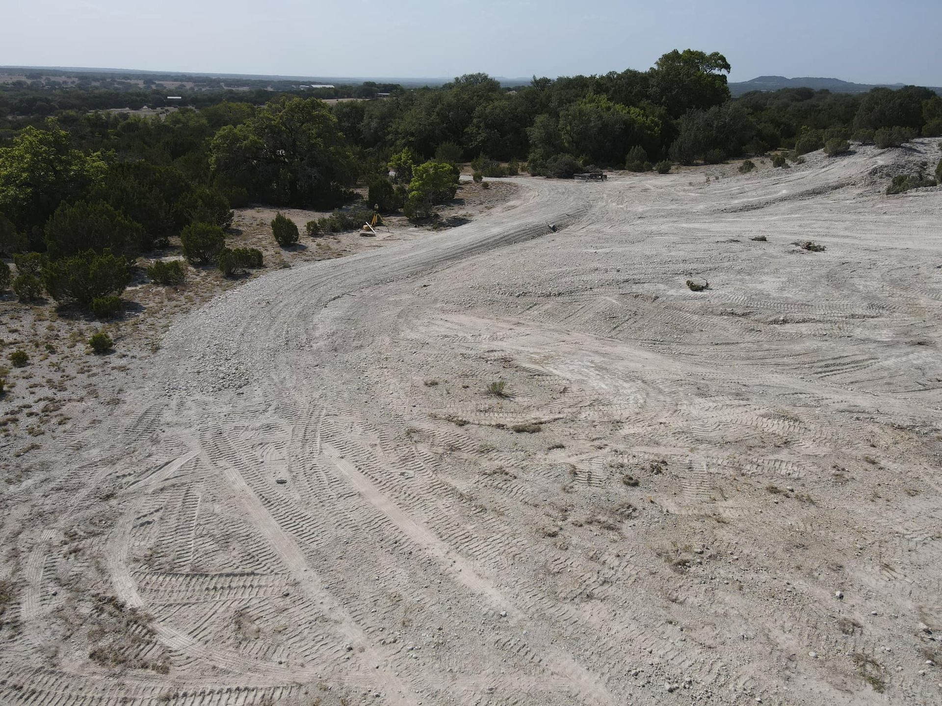 Sandy path with tire tracks, winding through a landscape with trees and a distant view.
