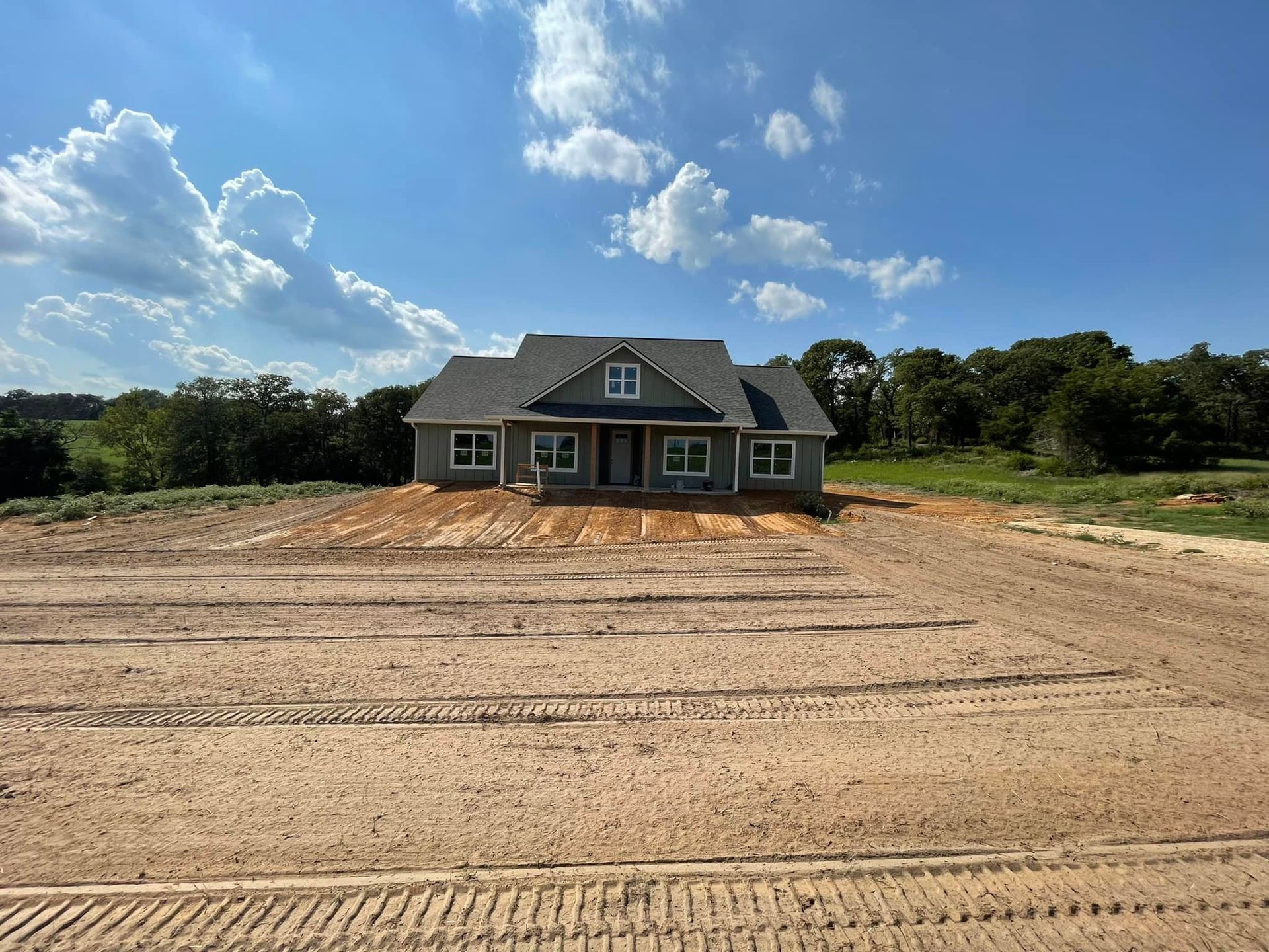 New house with gray siding on a sandy lot under a blue sky with clouds.