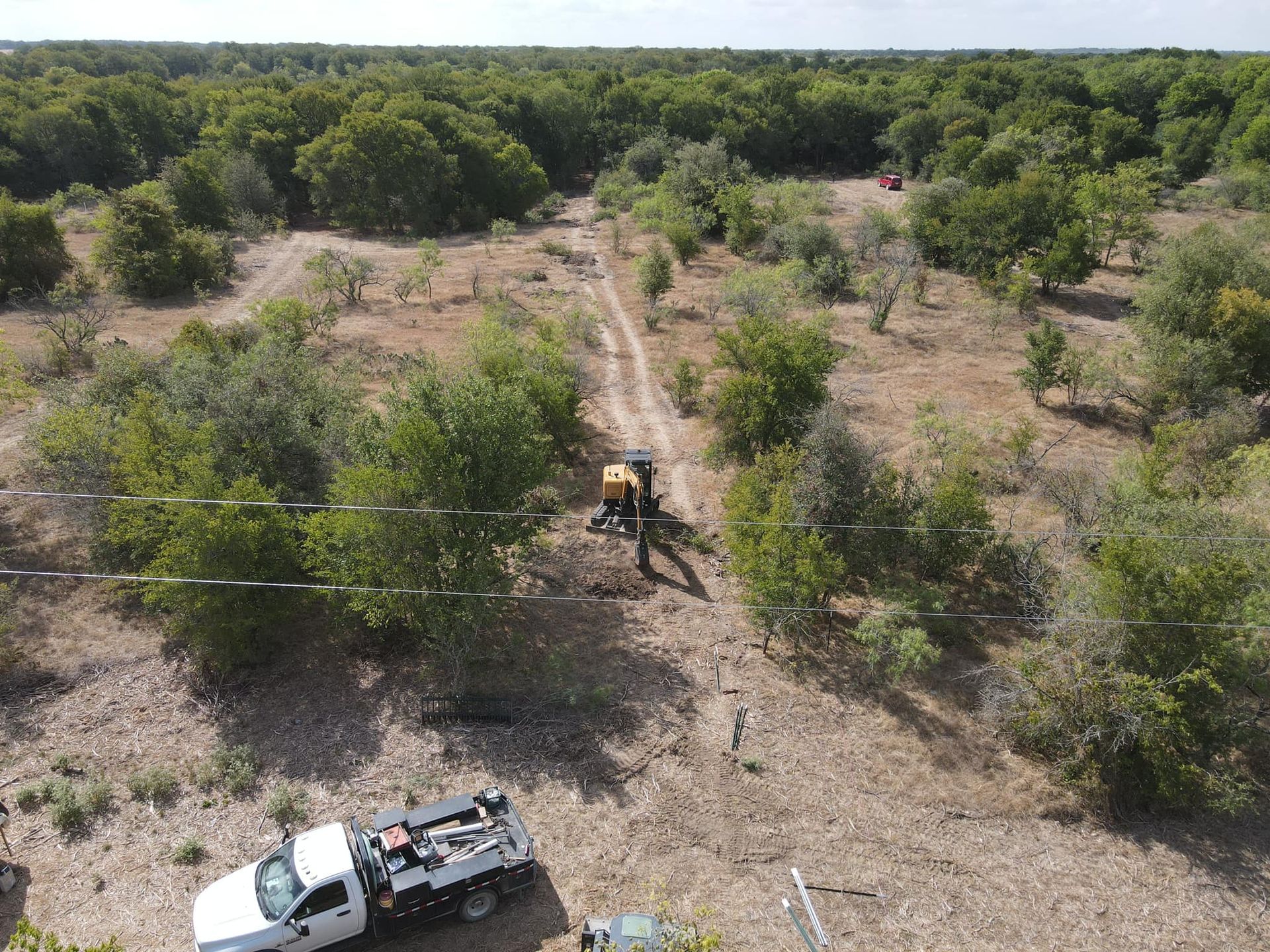 Aerial view of a dirt path through trees with a truck and tractor on the path.
