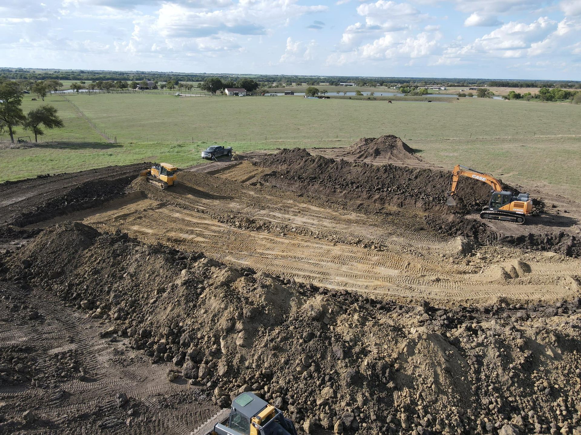 Construction site: Excavators digging earth in a field under cloudy skies.