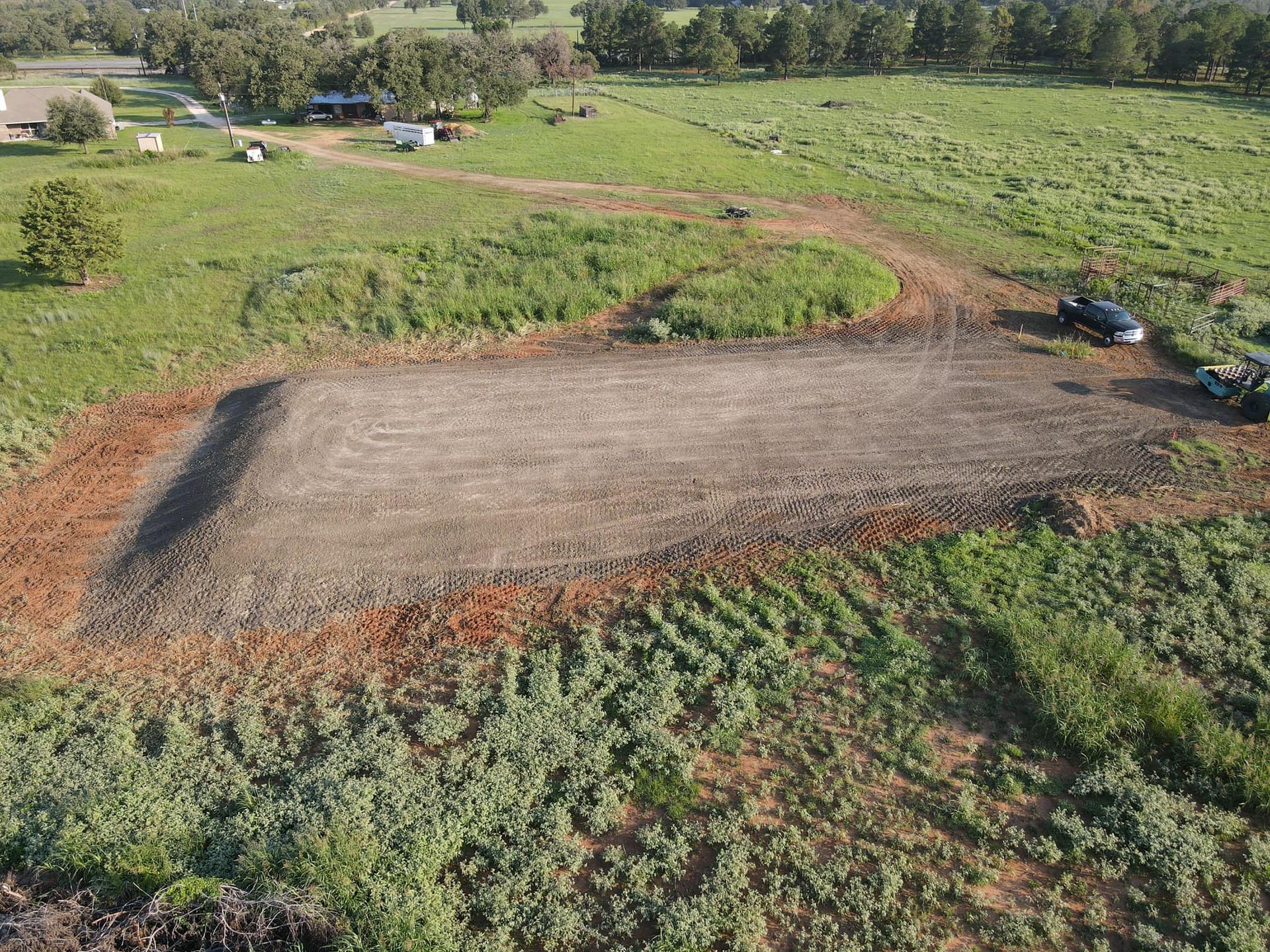 Aerial view of cleared land surrounded by grassy fields. A dark vehicle and equipment sit nearby.