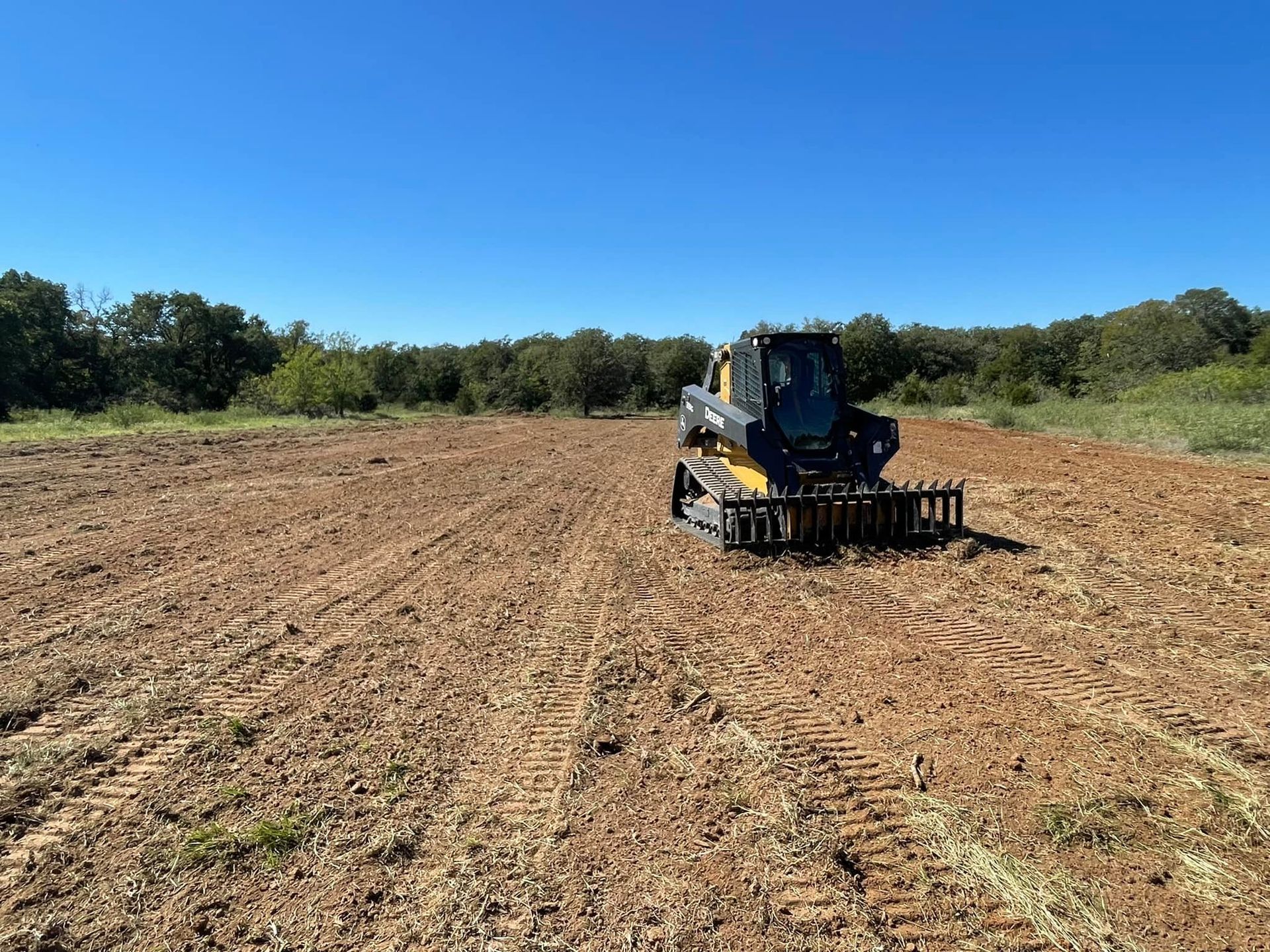 A small, yellow and black tractor with a tiller attachment tills a field under a blue sky.