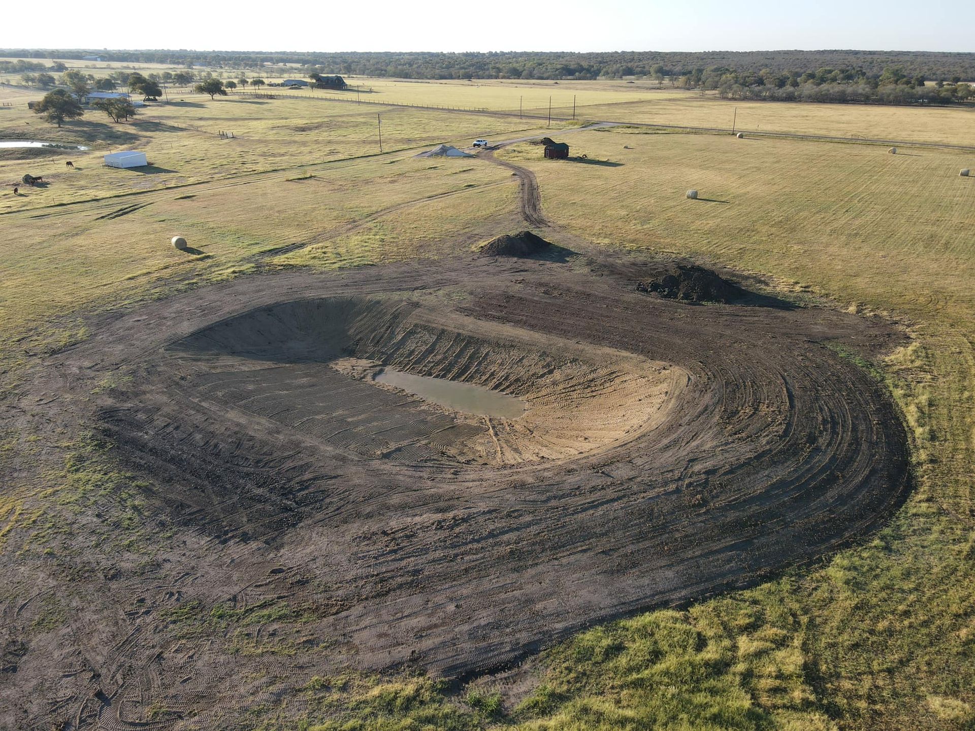 Earthworks project: A U-shaped earthen dam with a small pond, in a field under a clear sky.