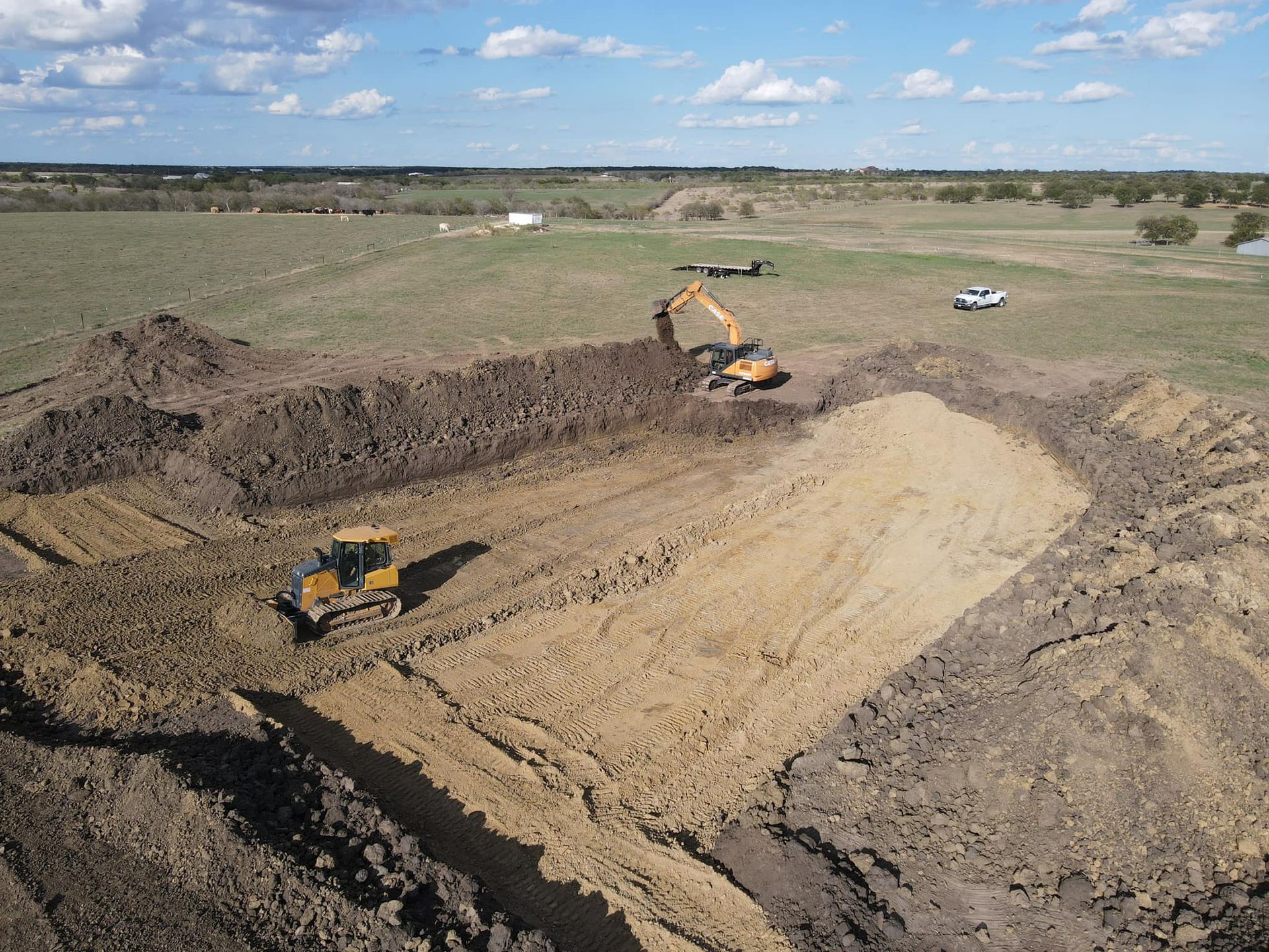 Construction site with excavators and a bulldozer digging into brown earth in a field.
