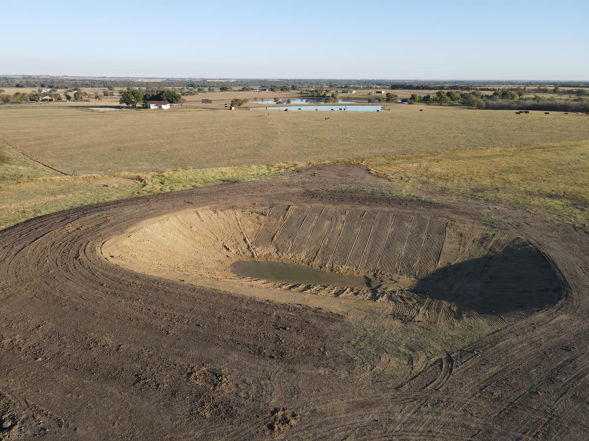 Aerial view of a freshly dug, circular pond in a field, with a small amount of water in the bottom.