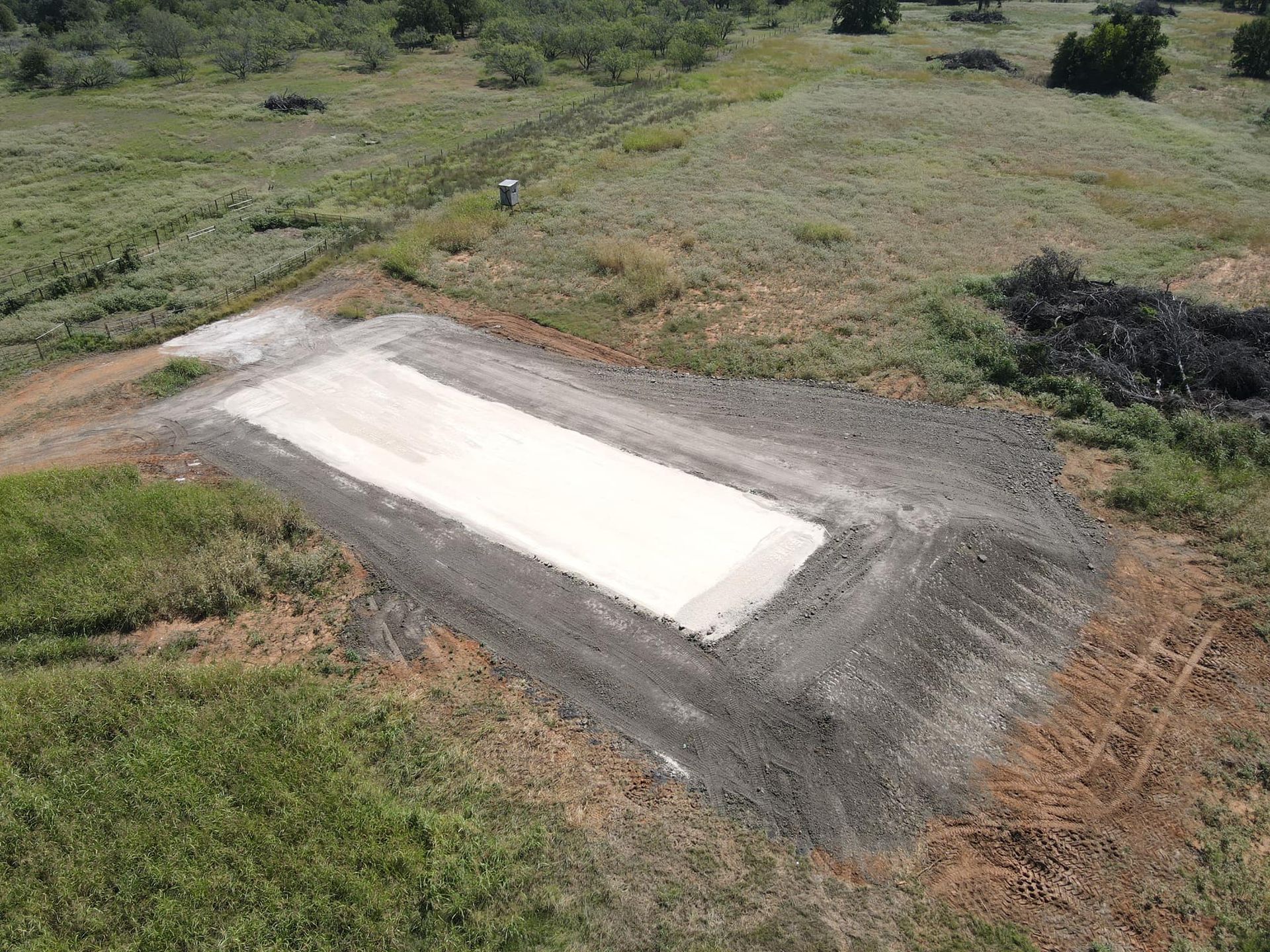 Aerial view of a rectangular concrete pad on a hill, surrounded by dirt and grass.