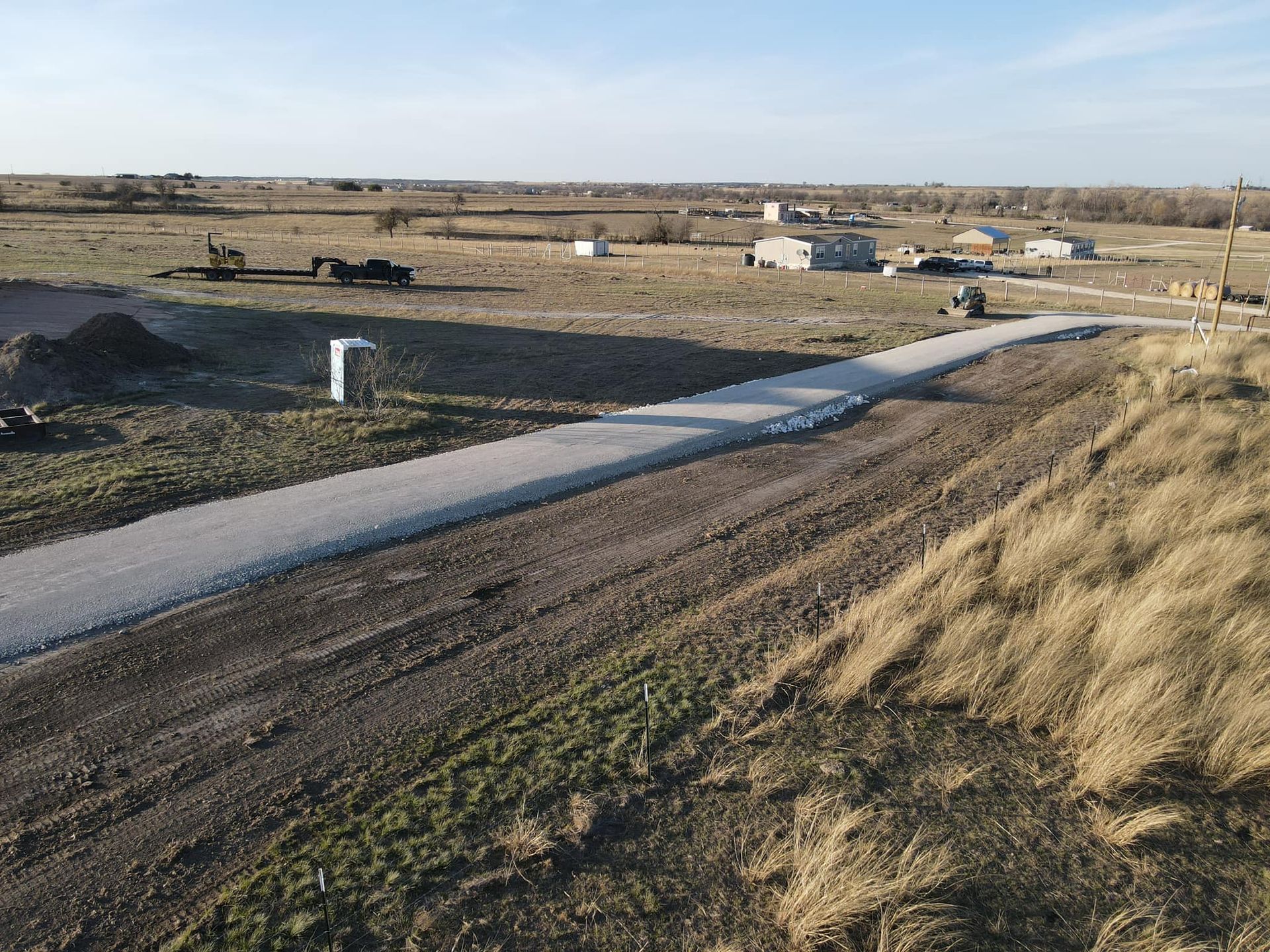 Gravel road through a rural area with sparse buildings under a clear sky.