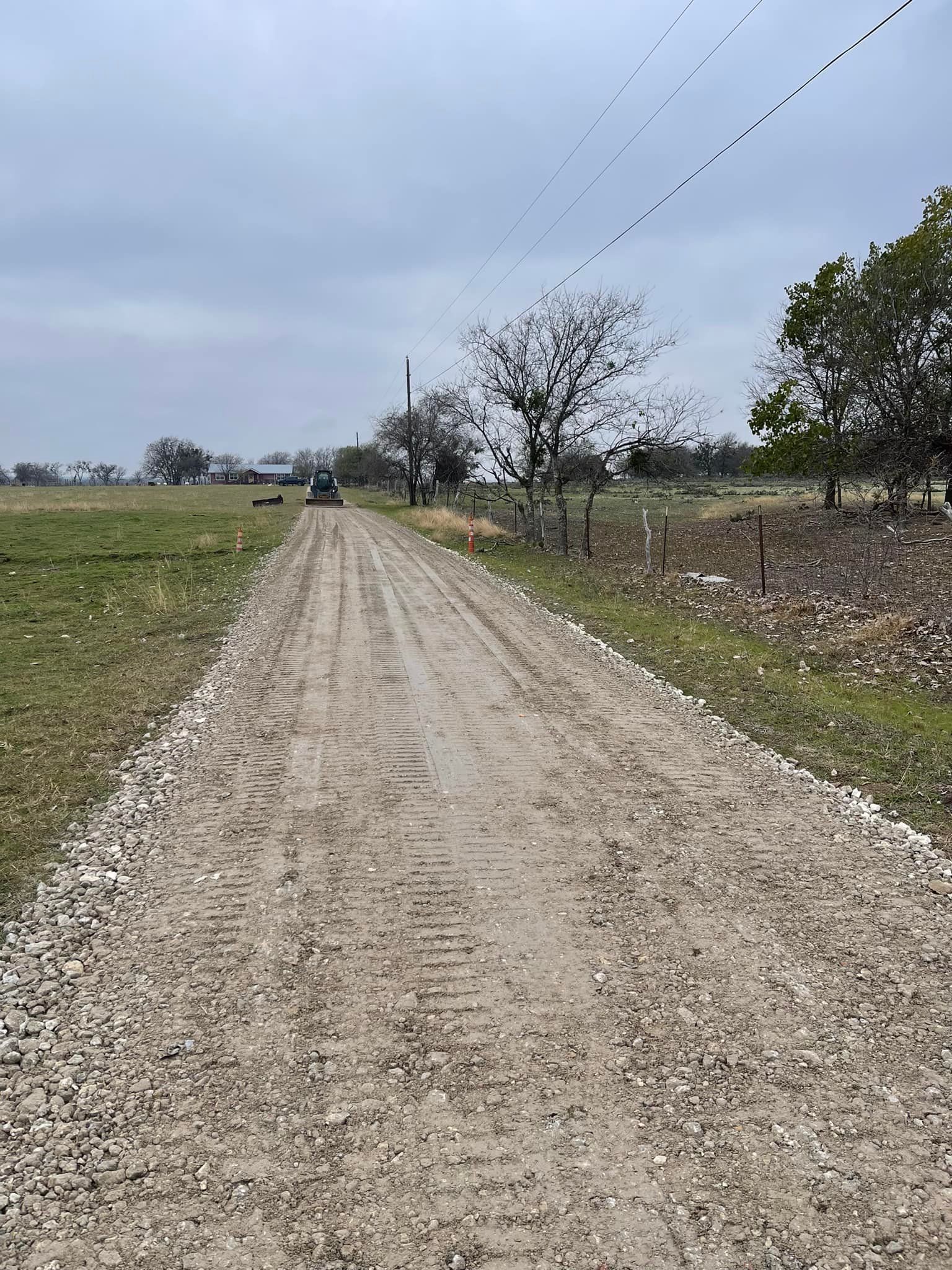 Gravel road leading through a field under a cloudy sky. A vehicle is visible in the distance.
