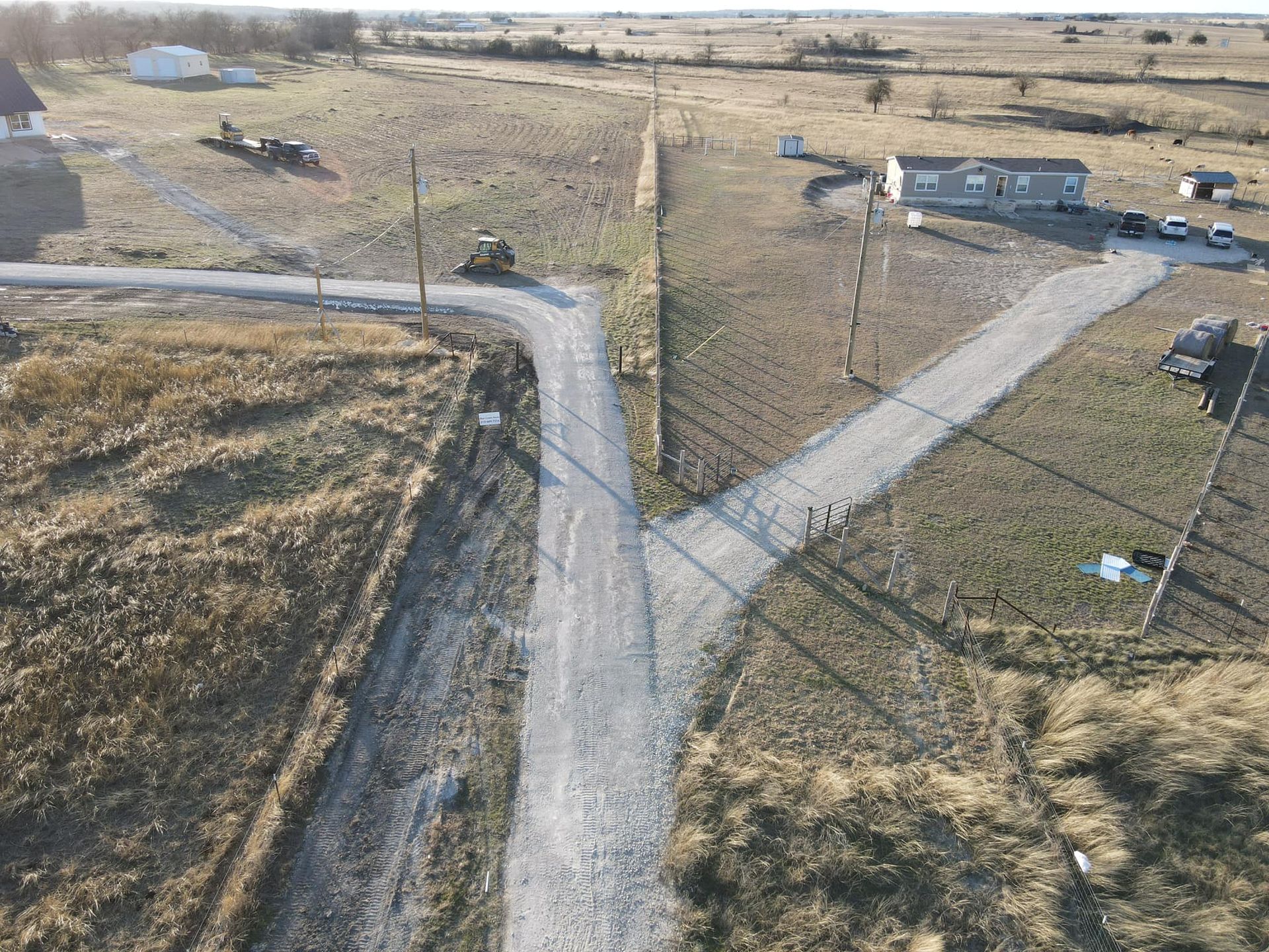 Gravel roads split in two across a field. A small building sits in the distance. Overcast sky.