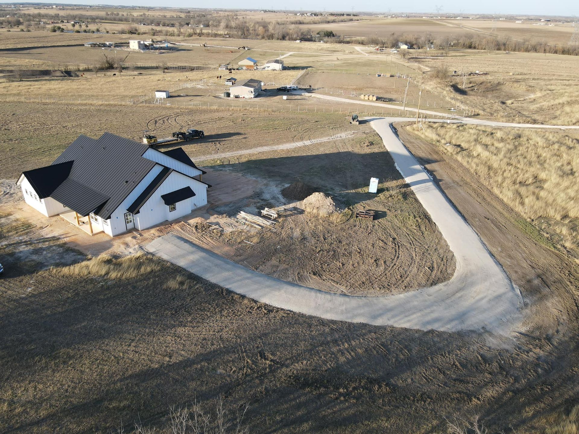 A newly constructed white house with a black roof and a curved driveway in a rural setting.
