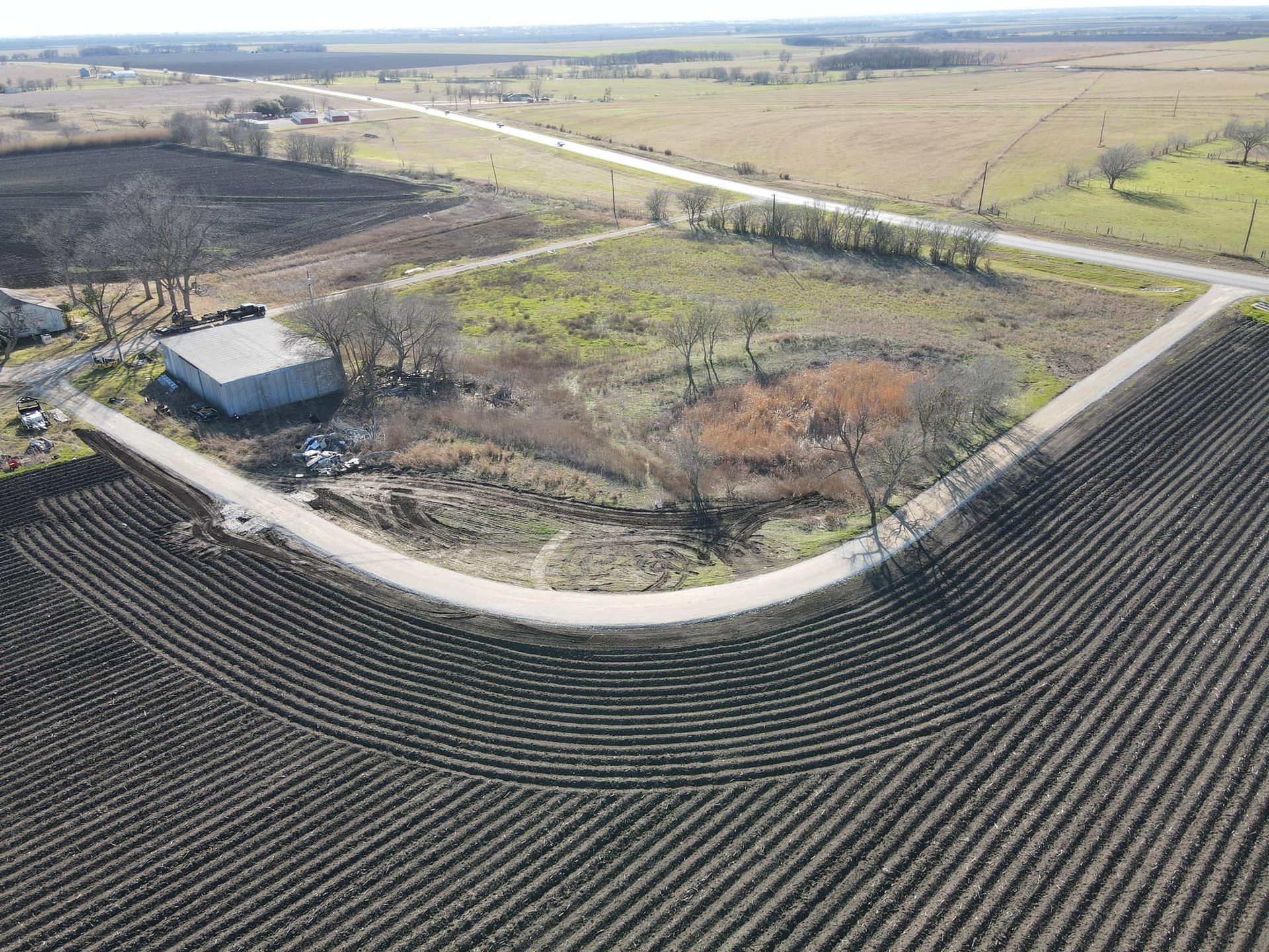 Aerial view of rural landscape with a curved road, field, and a building.
