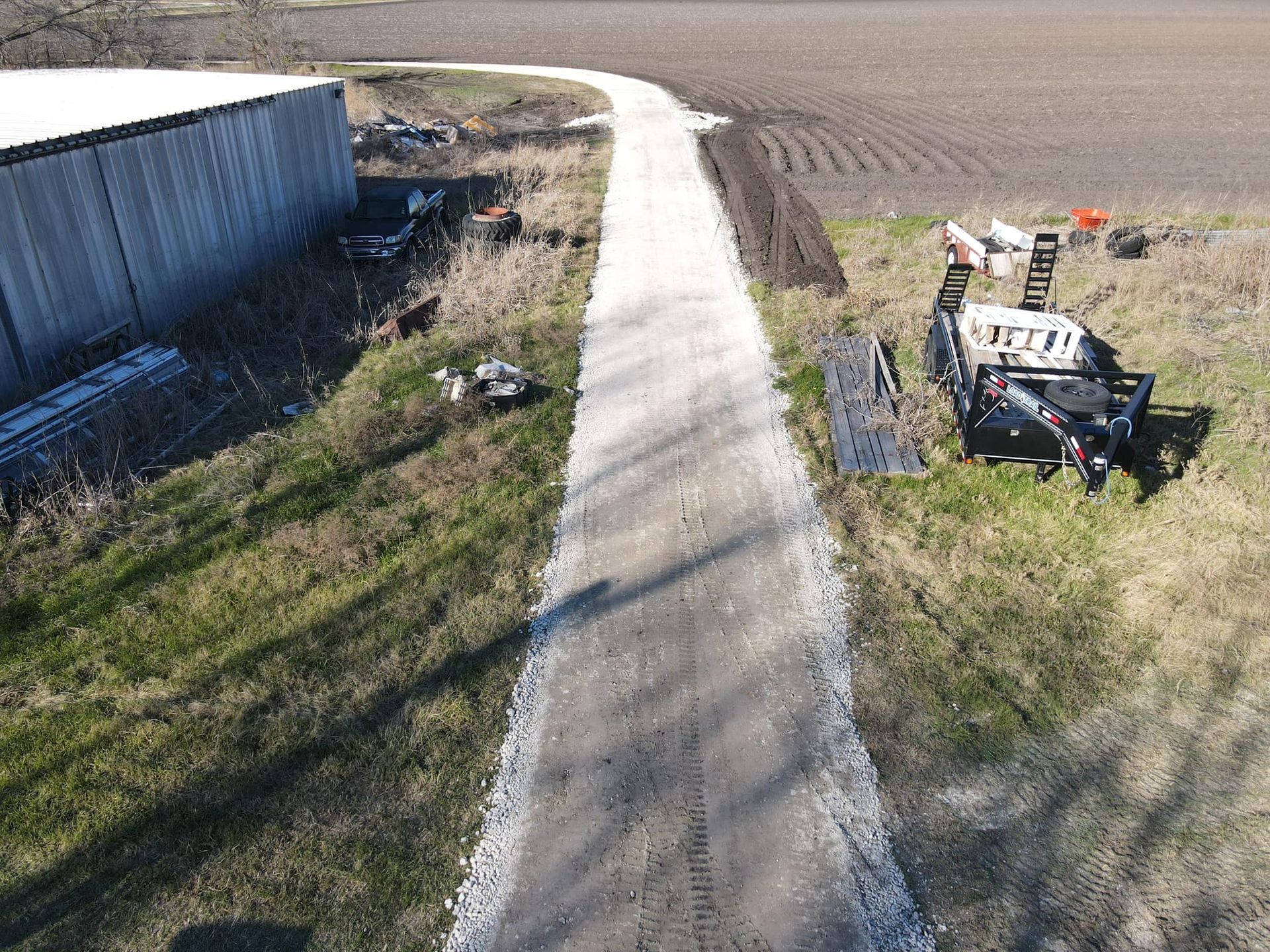 Gravel driveway beside a barn and field. A vehicle and debris are along the side.