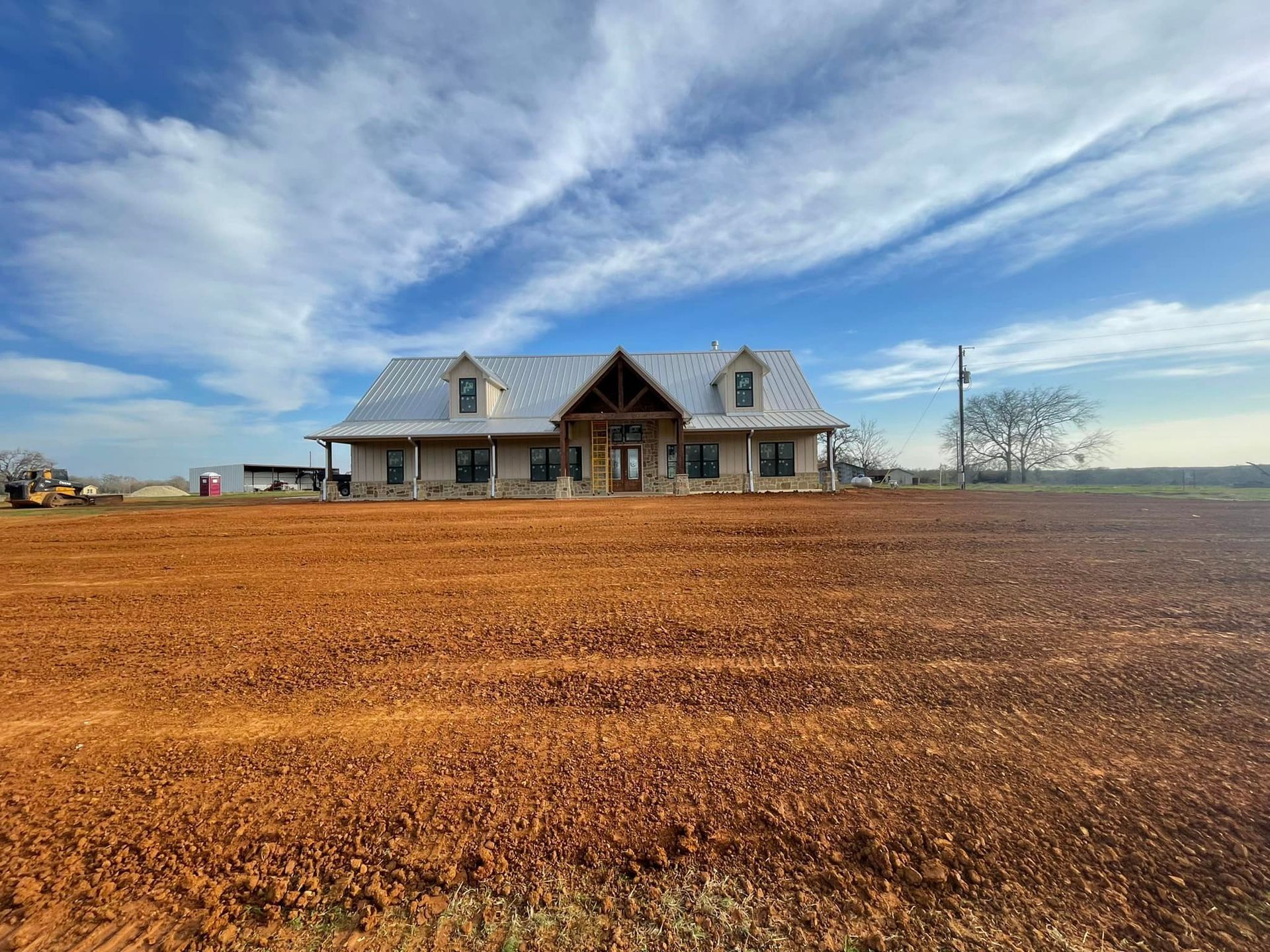 Large farmhouse on a plowed, brown field under a blue sky with wispy clouds.