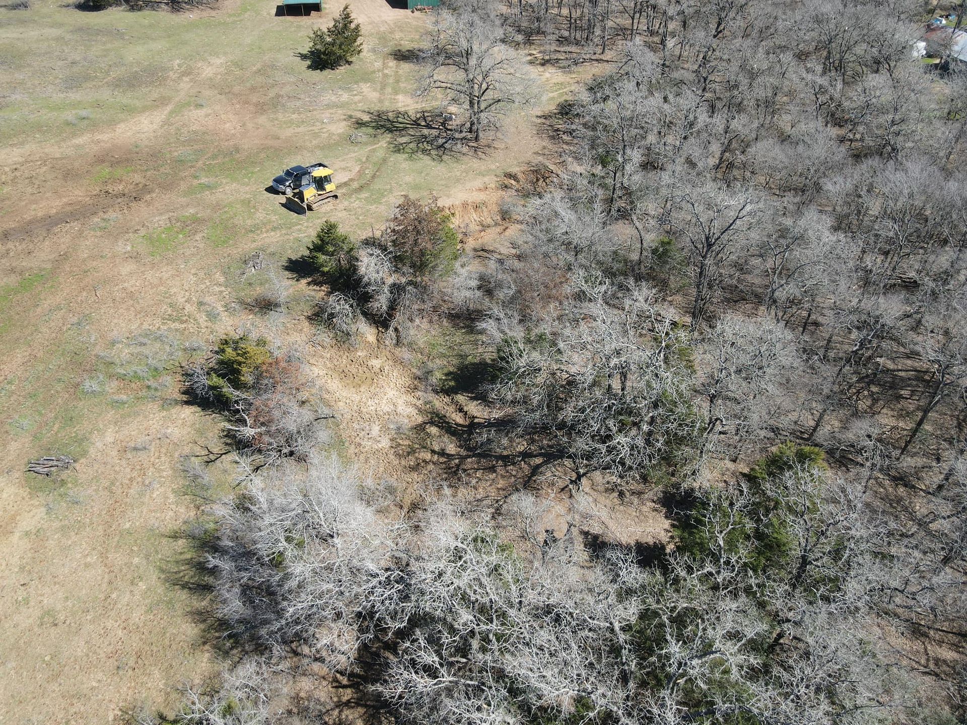 Aerial view of a field with sparse trees. Two people stand near a vehicle. Brown and green tones.