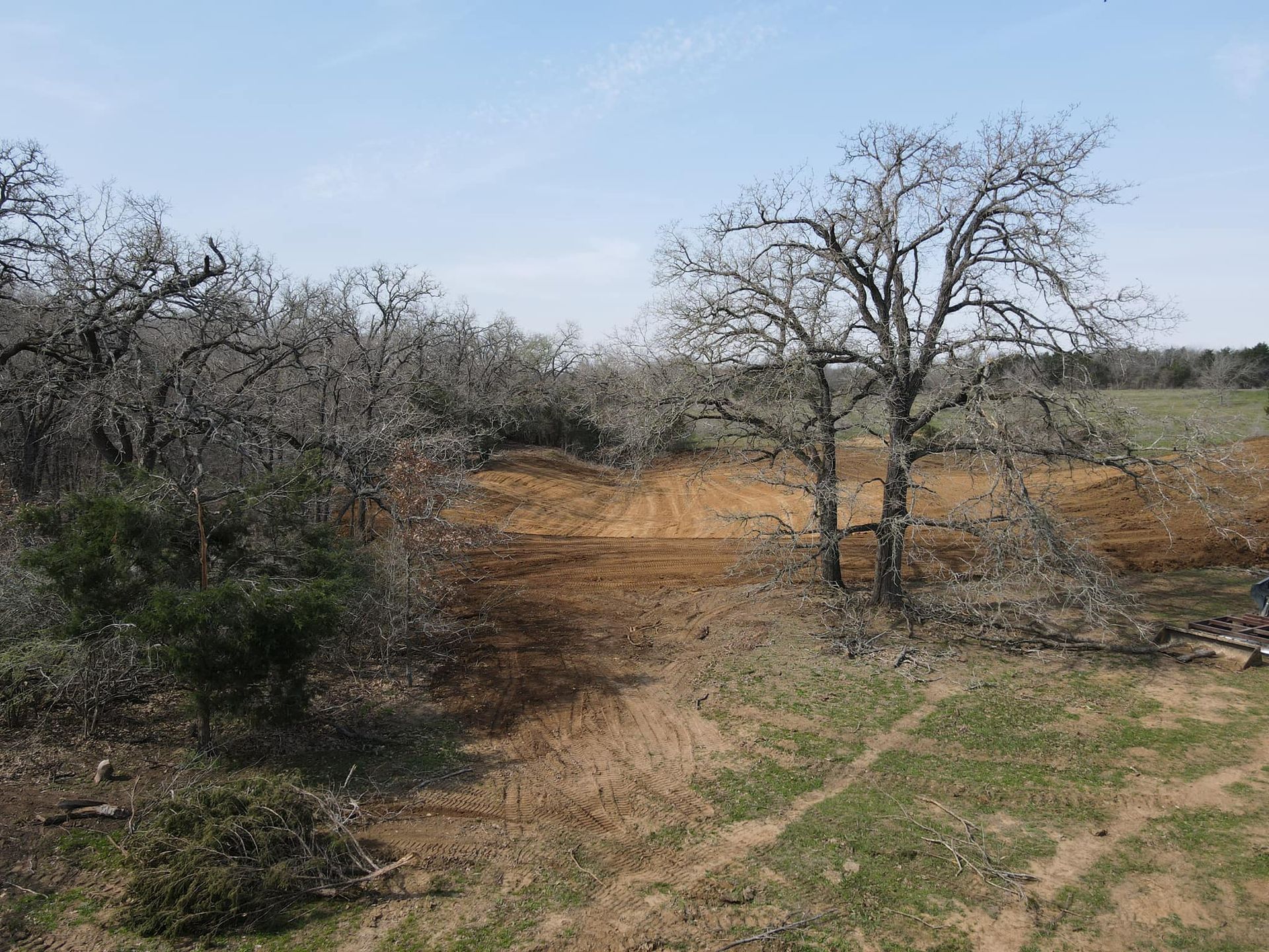 Brown and green landscape with bare trees, a cleared dirt area, and a blue sky.