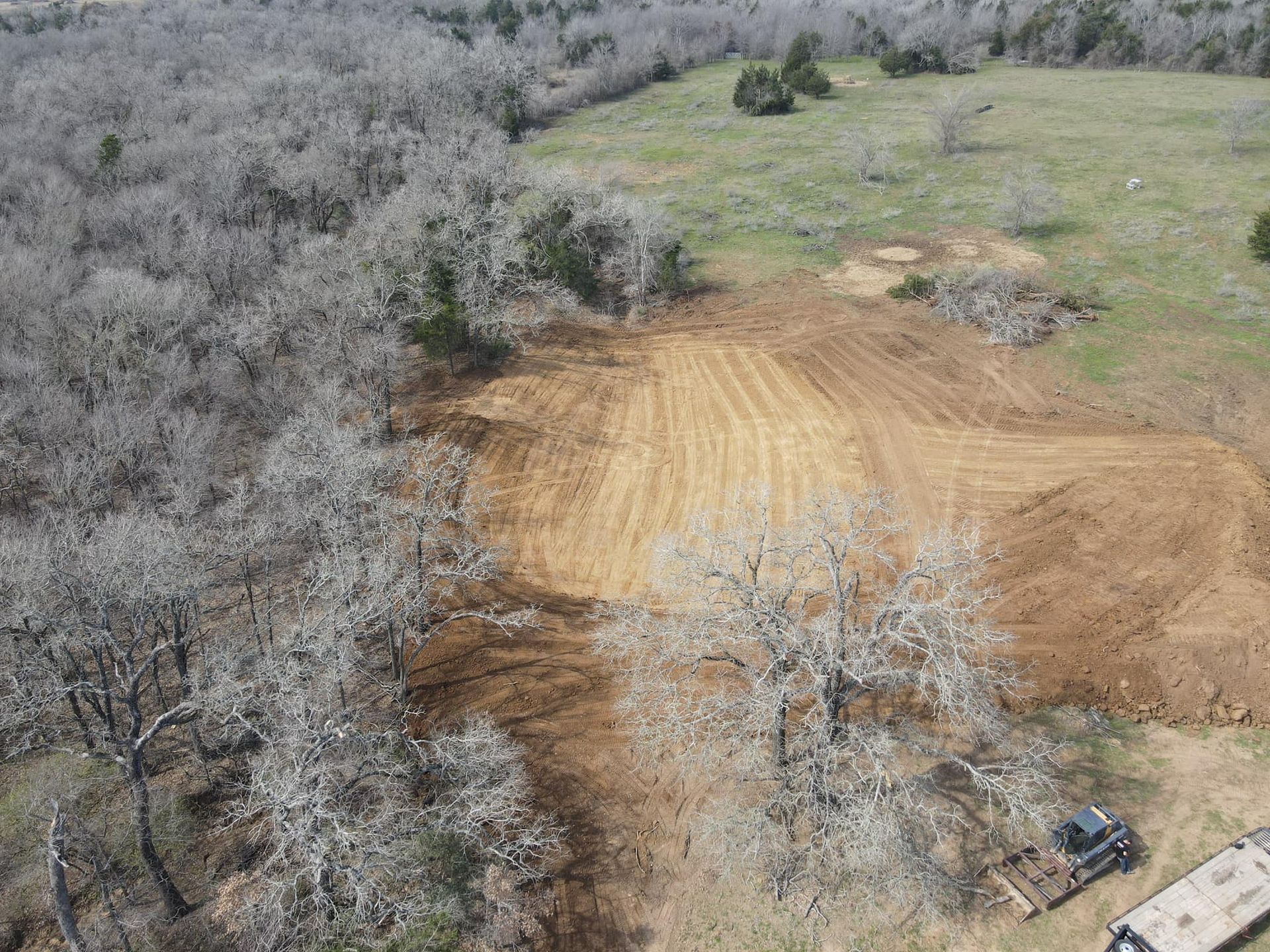 Aerial view: freshly tilled brown earth cleared beside a forest of bare trees and a grassy field.