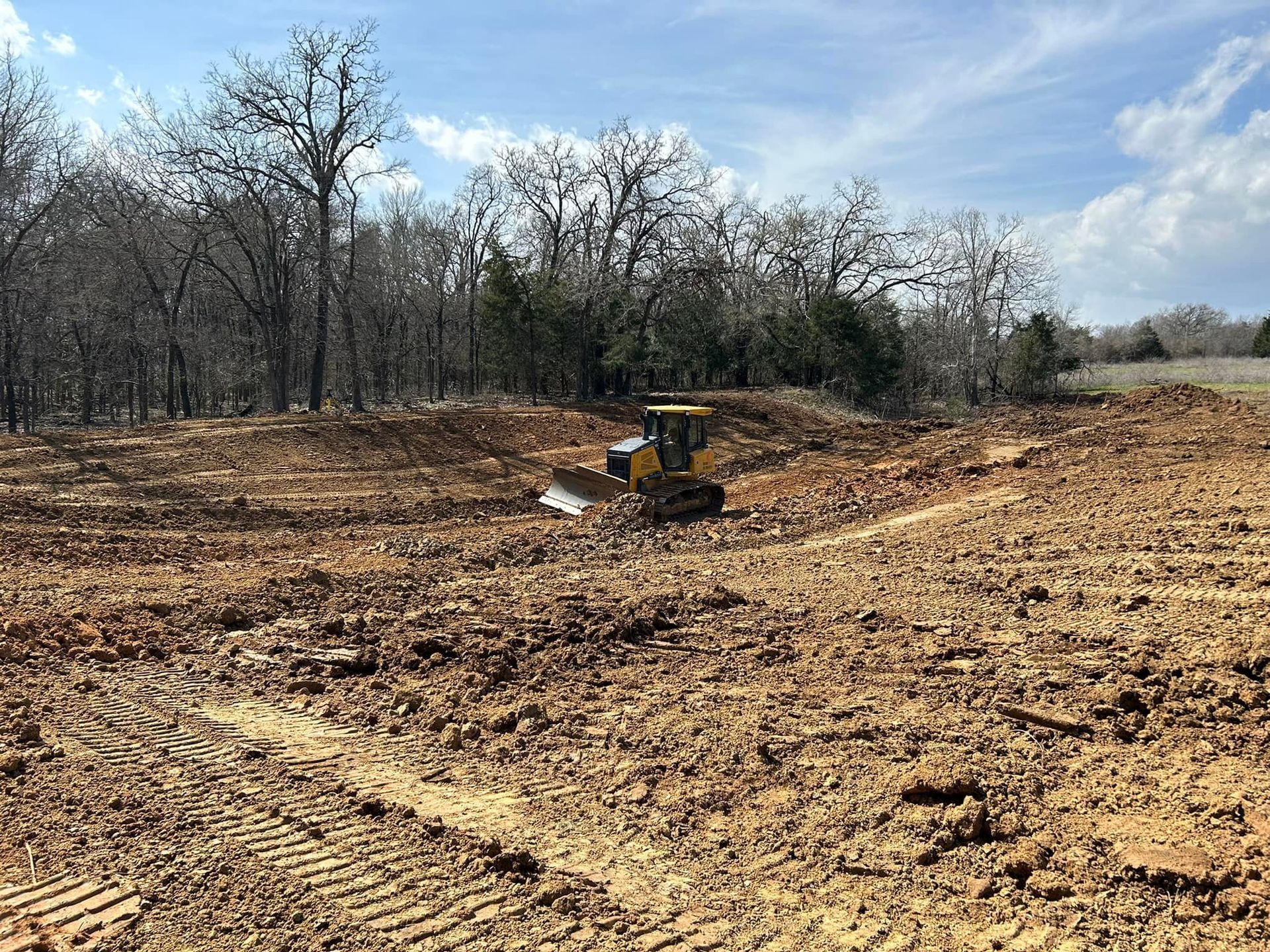 A bulldozer clearing land in a dirt field, with trees in the background under a blue sky.